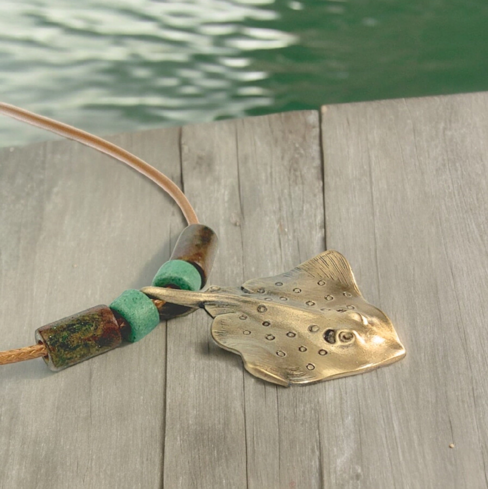 Brass fish-shaped pendant on a wooden surface with water in the background