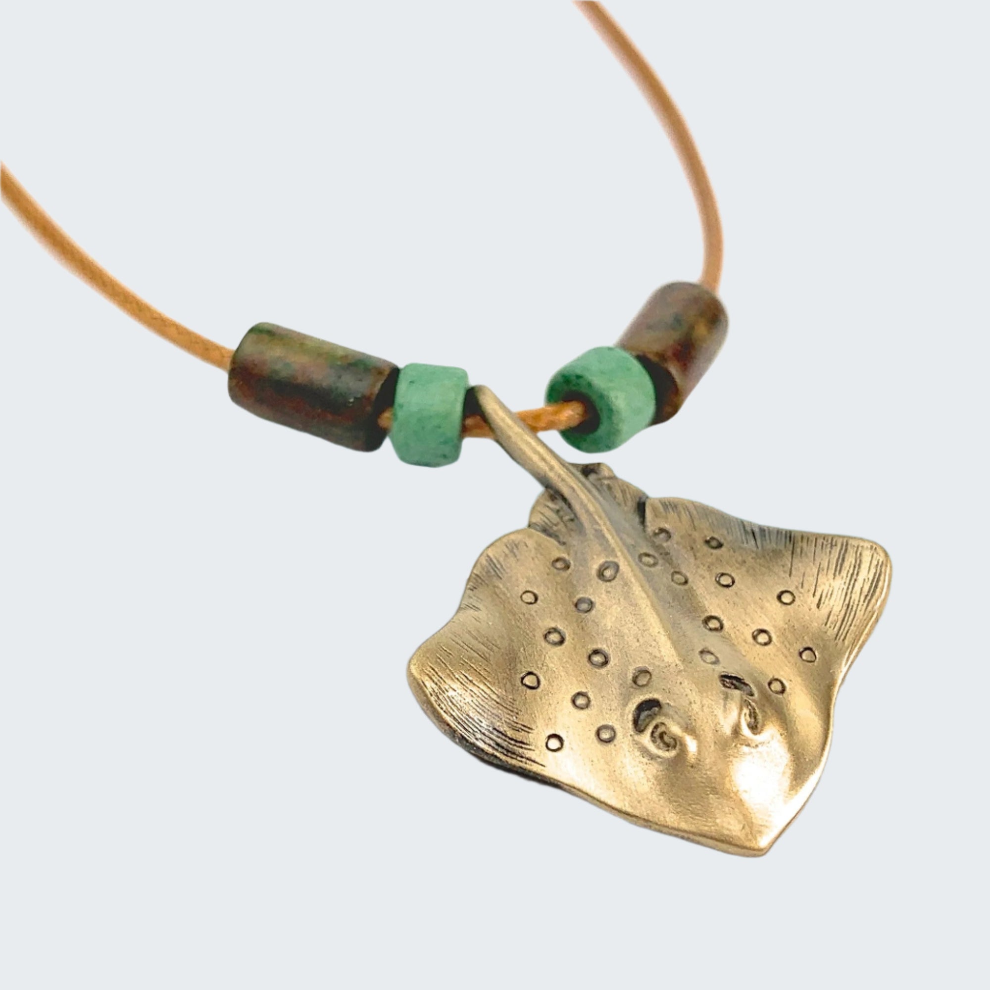Gold stingray pendant necklace with green beads on a light gray background