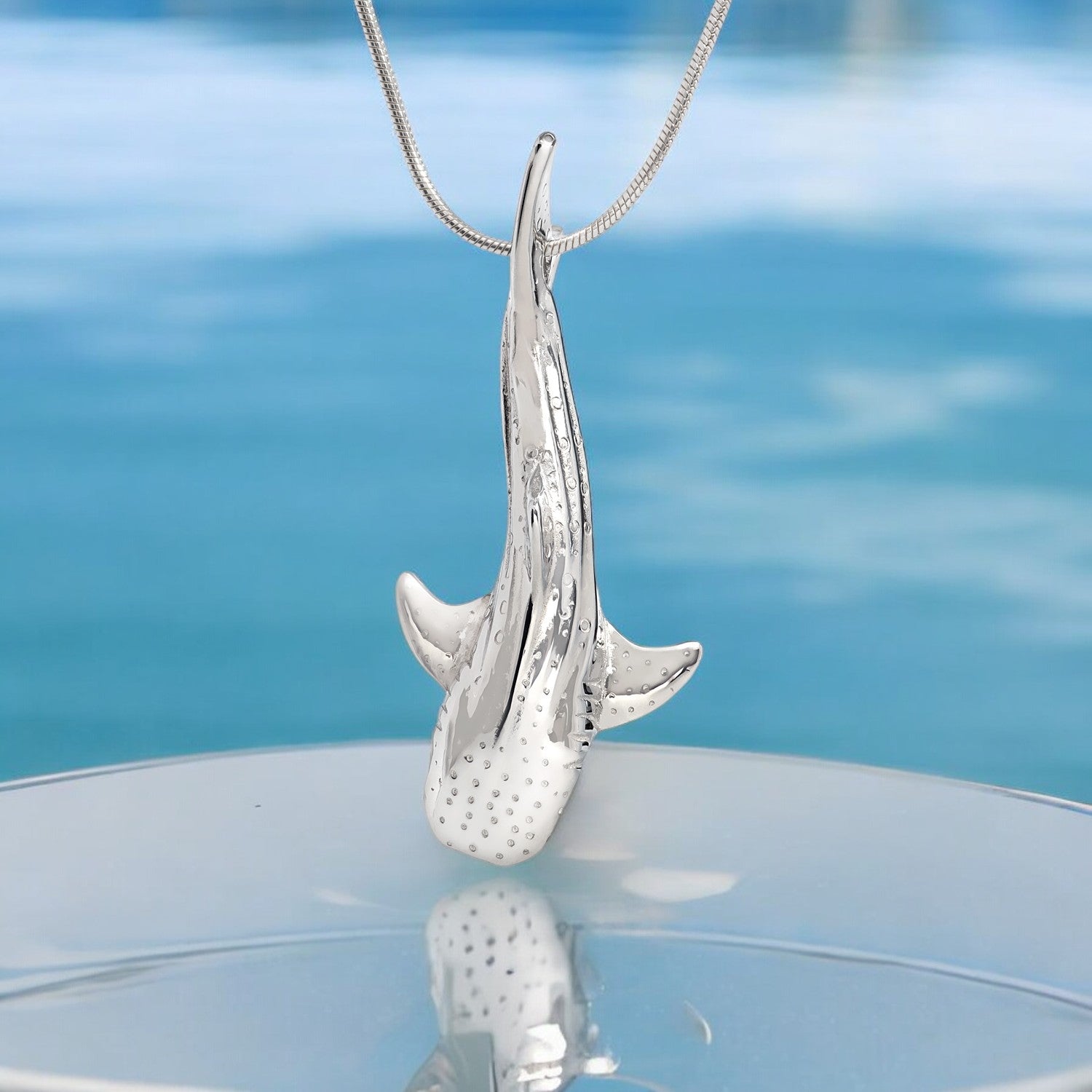 Silver shark pendant on a chain against a blue water background