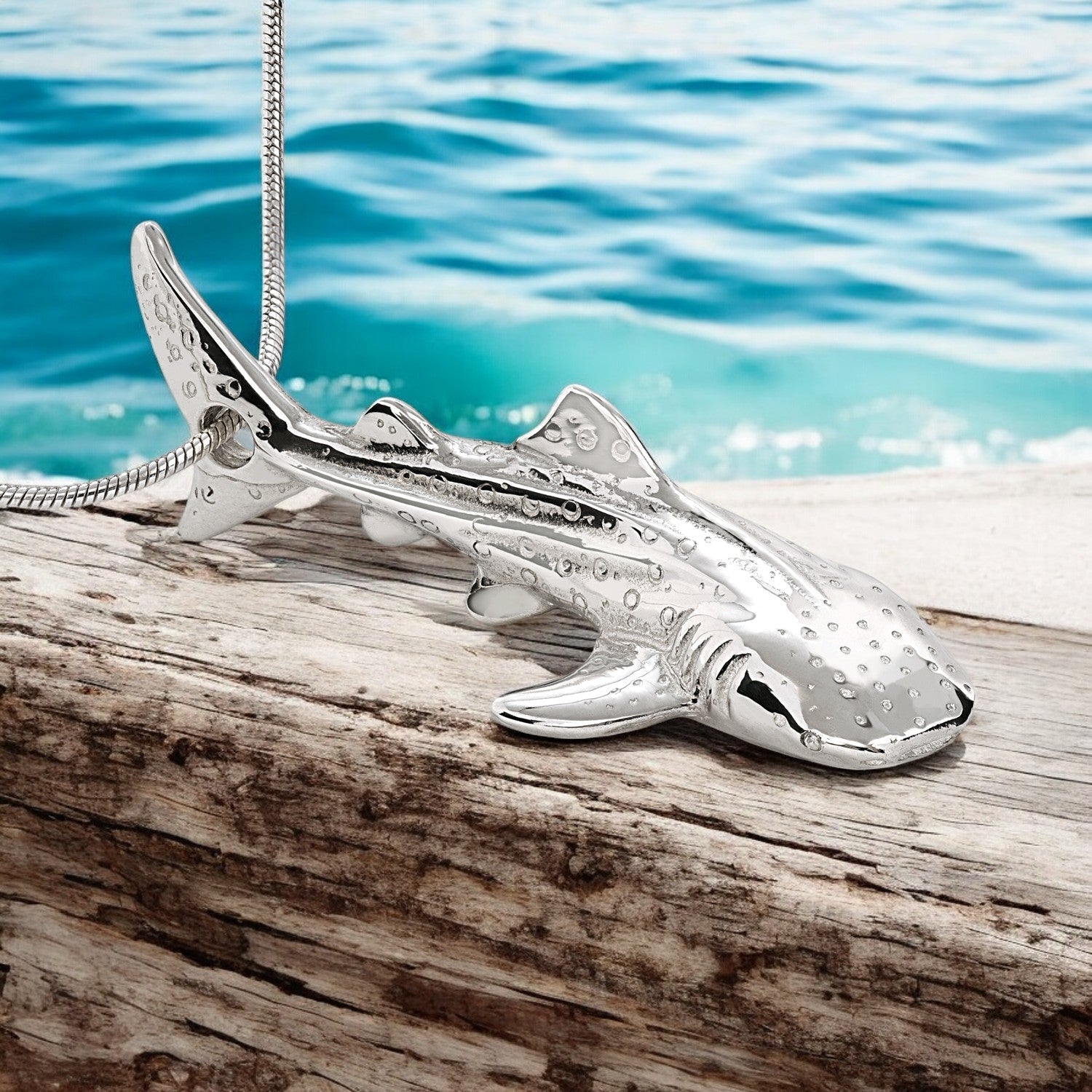Silver shark pendant on a wooden surface with water in the background