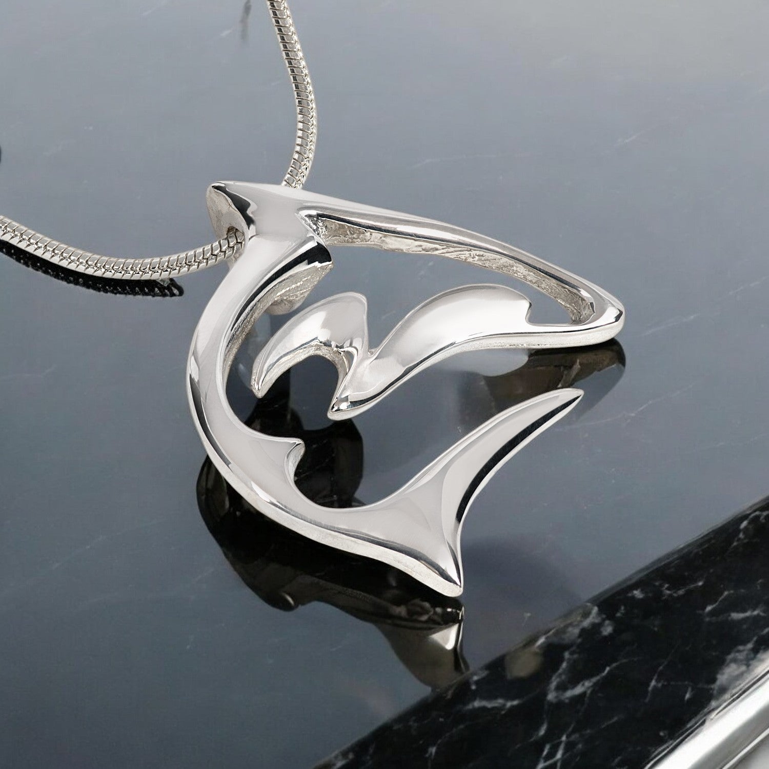 Silver dolphin pendant on a reflective surface
