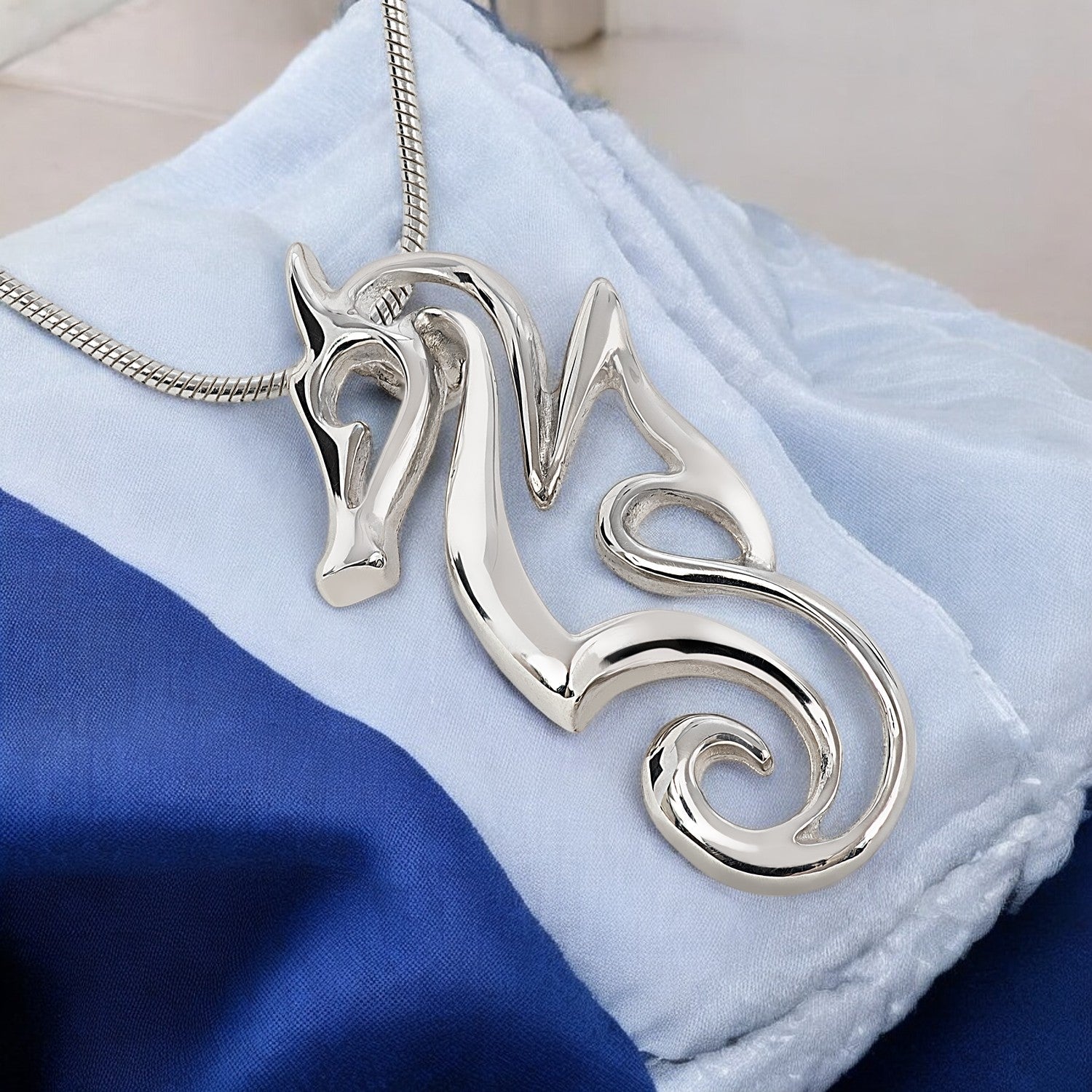 Silver seahorse pendant on a blue and white fabric background