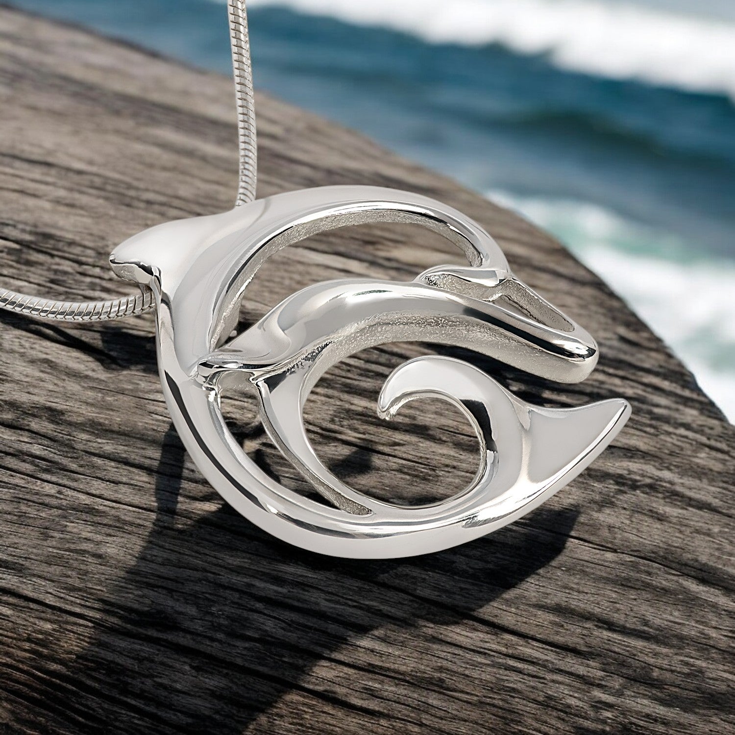 Silver dolphin pendant on a wooden surface with ocean in the background