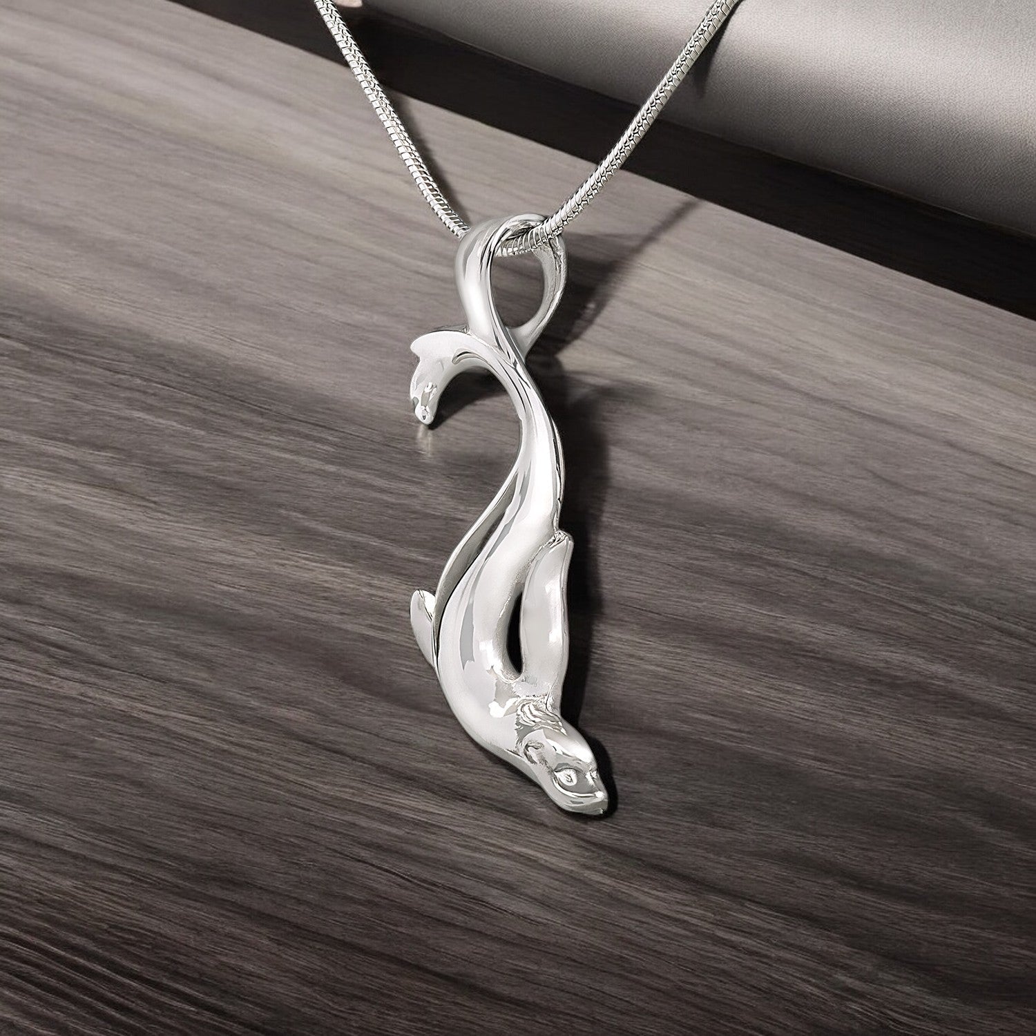 Silver pendant shaped like a stylized animal on a wooden surface