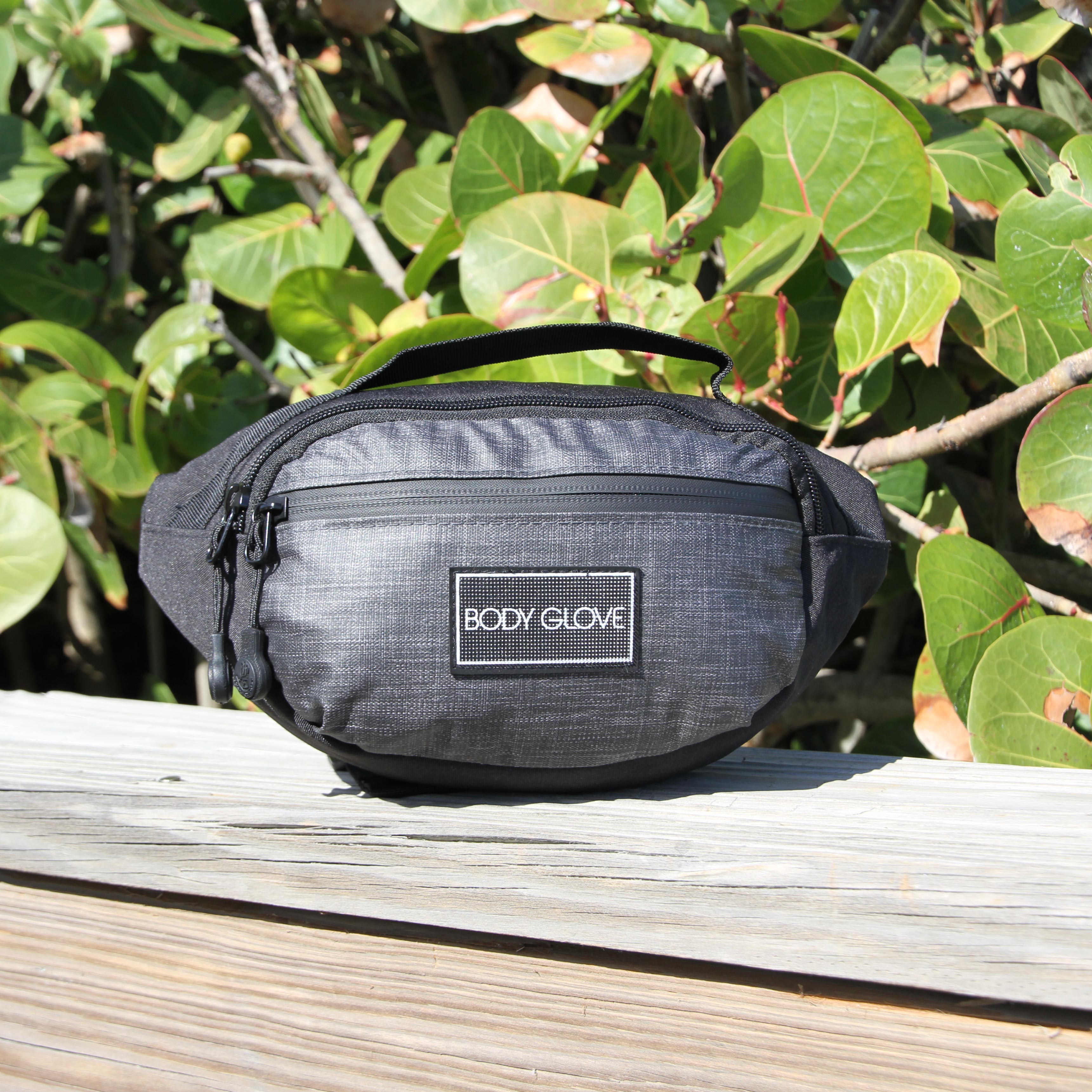 Black waist bag with 'Body Glove' logo on a wooden surface with green foliage in the background