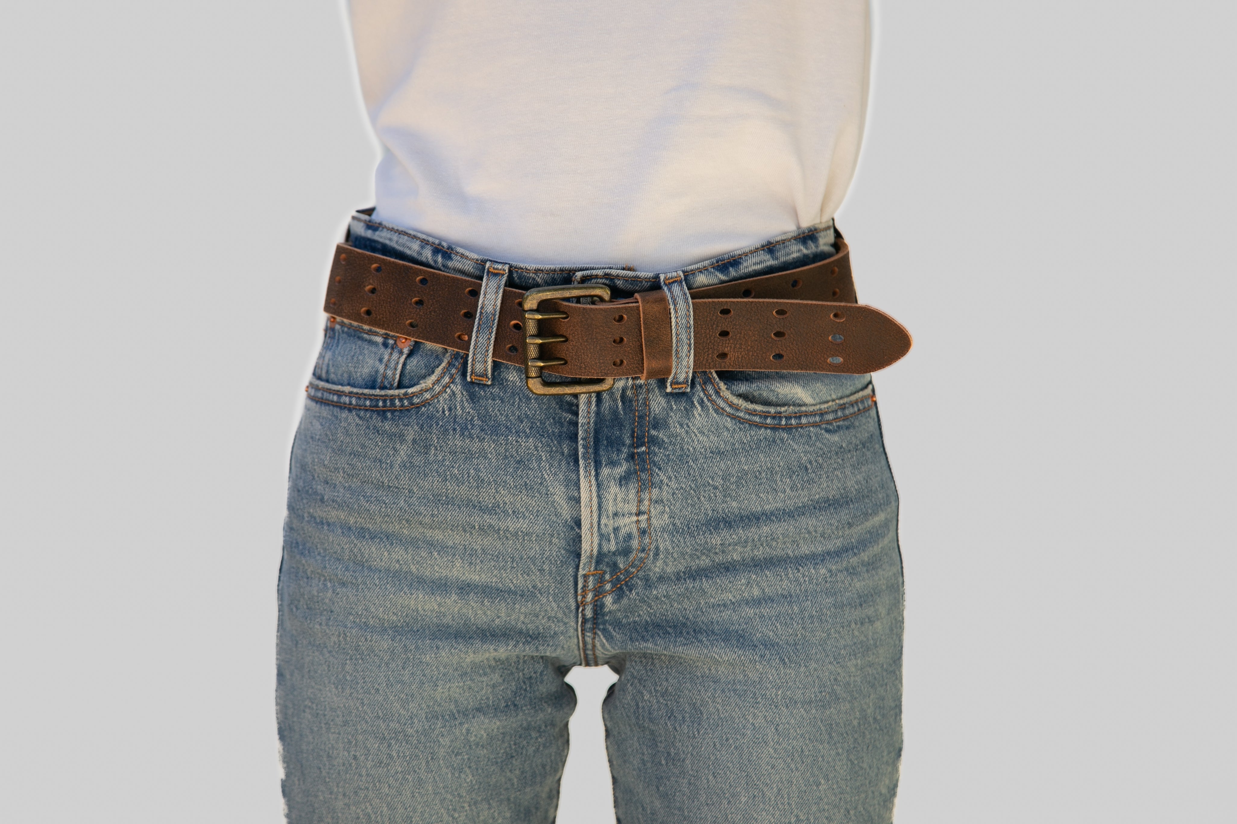 Mannequin wearing blue jeans with a brown belt on a plain background