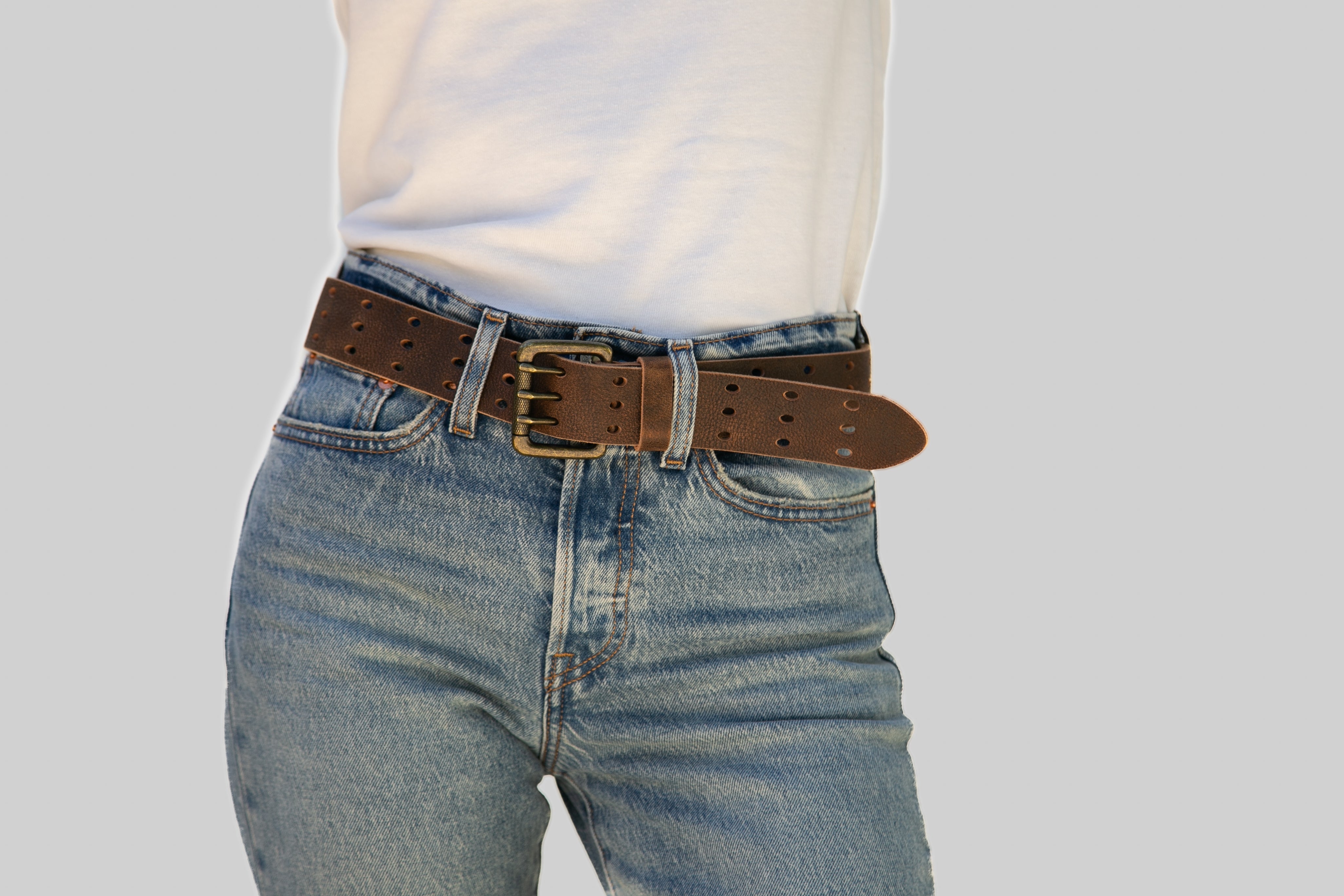 Person wearing blue jeans with a brown belt on a light gray background