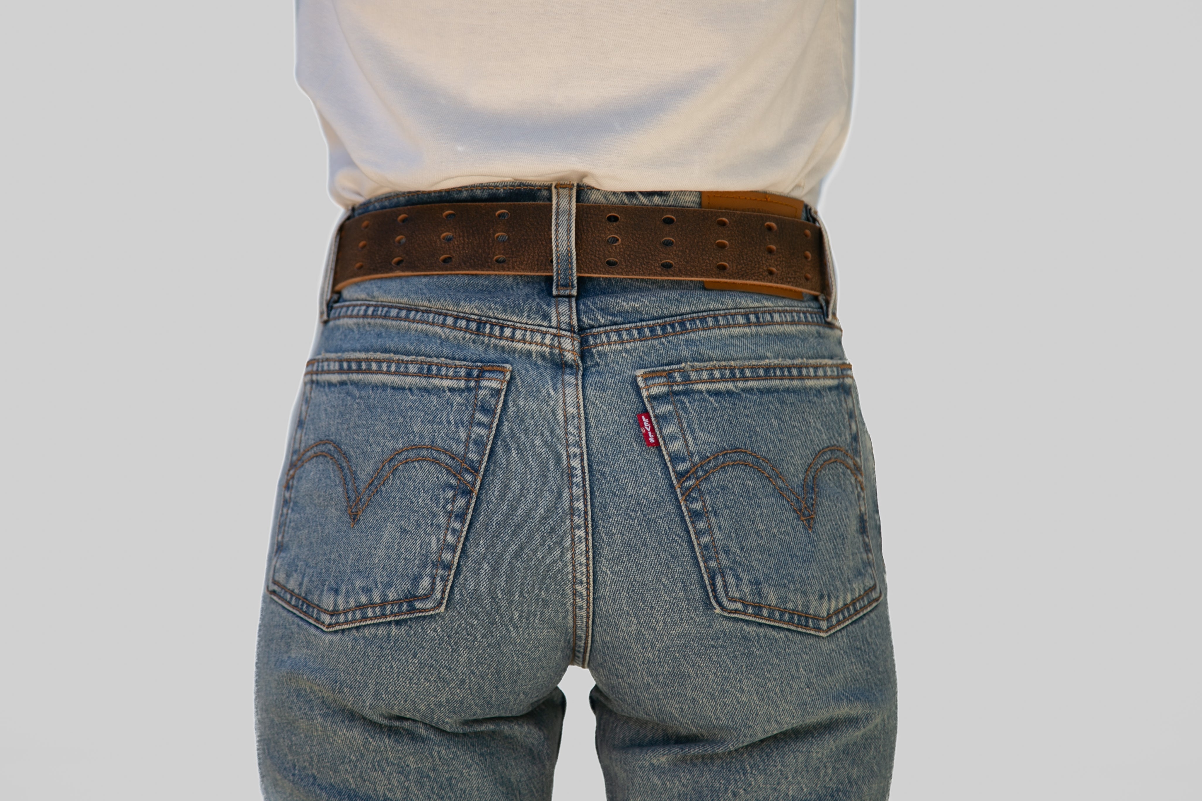 Blue jeans with a brown belt on a plain background