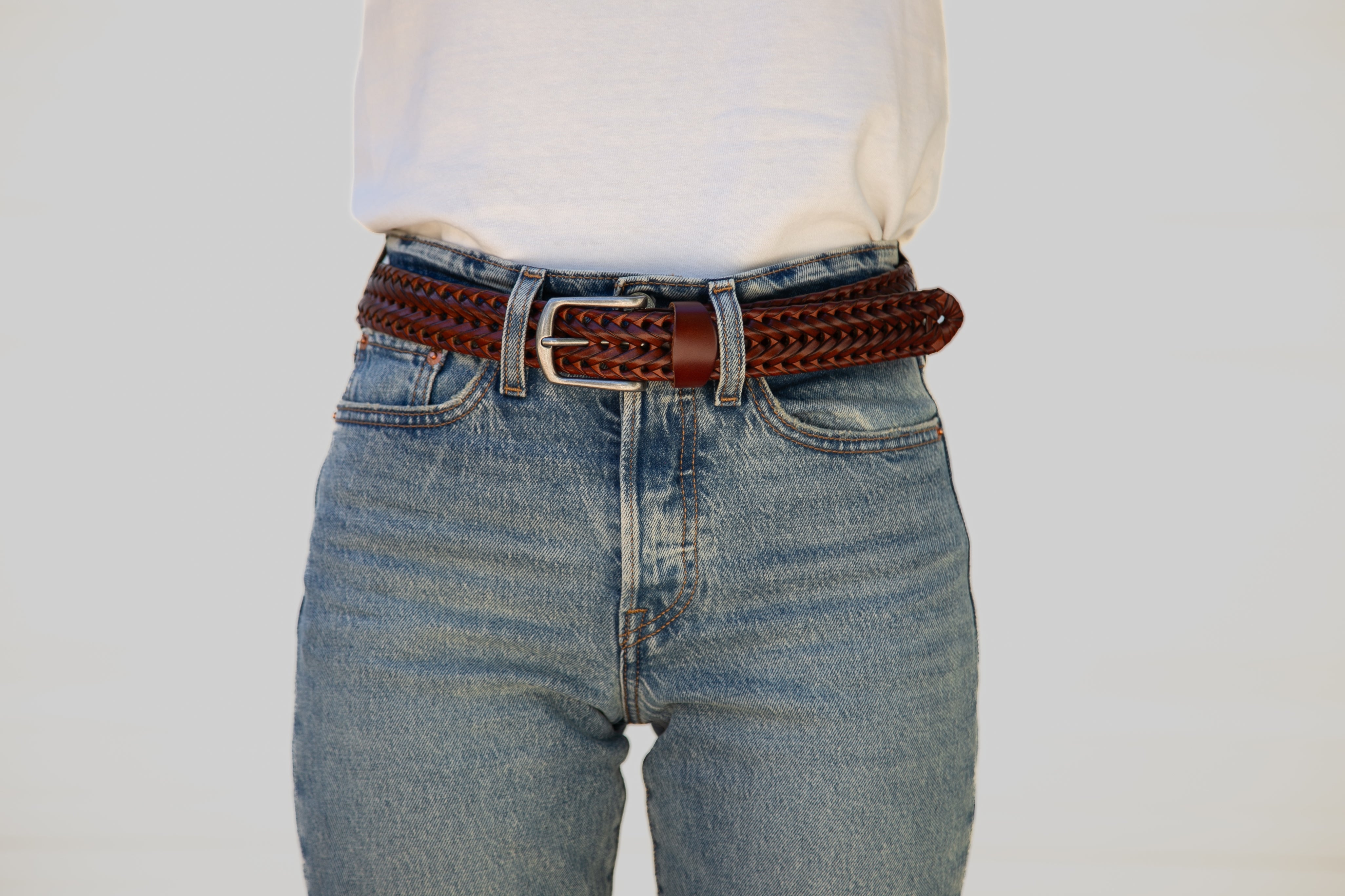 Person wearing blue jeans with a brown leather belt on a plain background