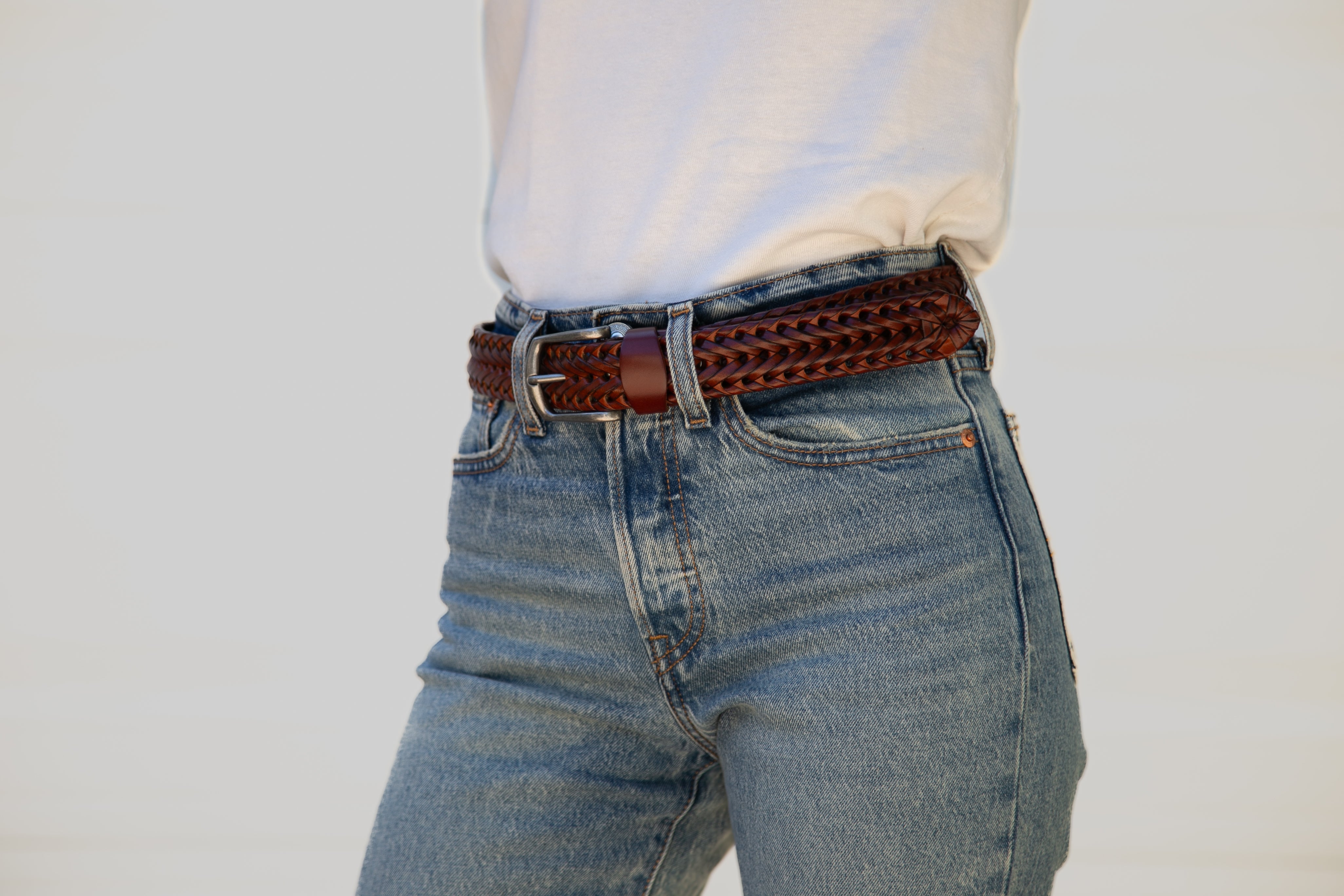 Person wearing blue jeans with a brown belt on a plain background