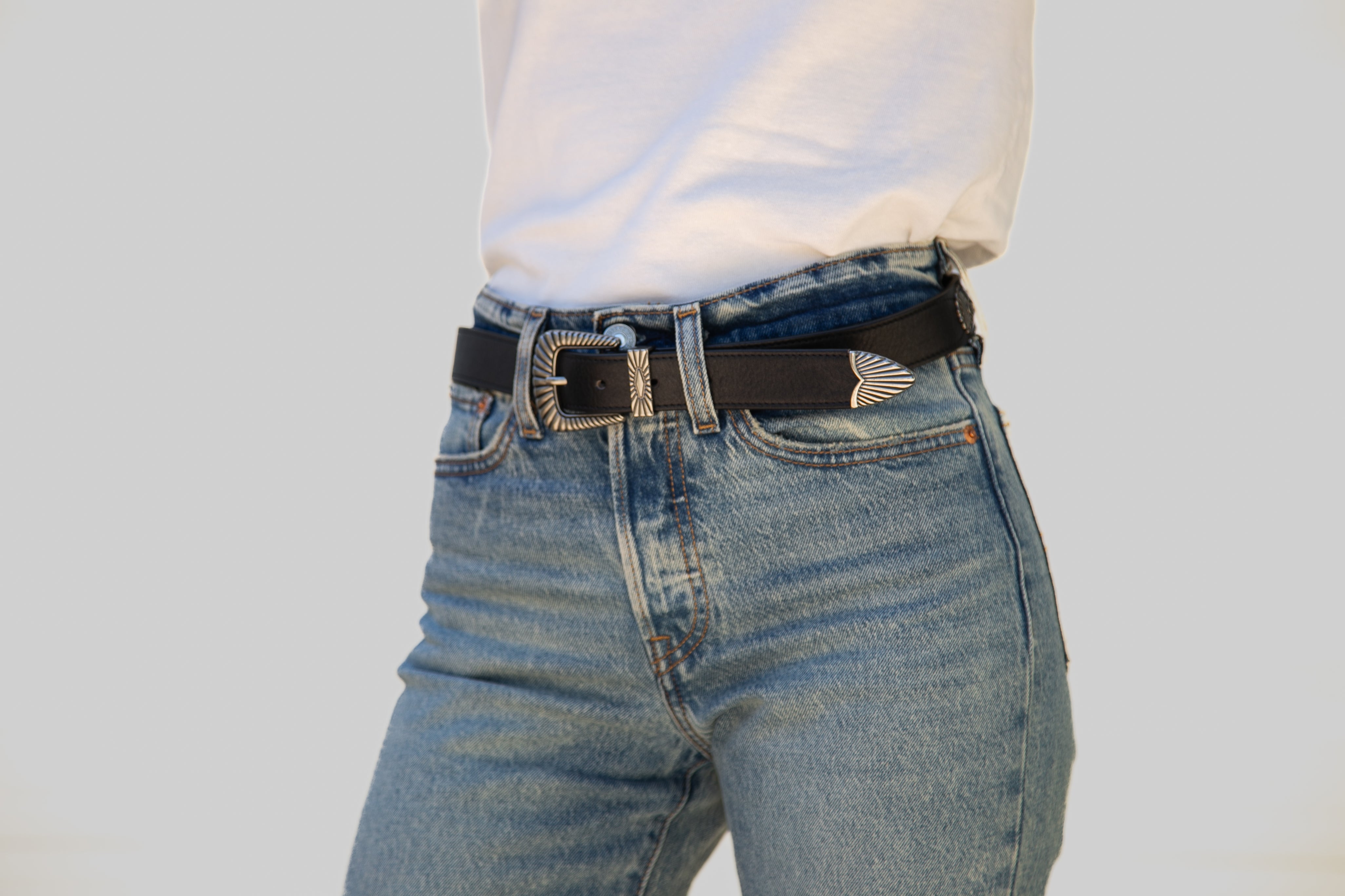 Person wearing blue jeans with a black belt on a light gray background