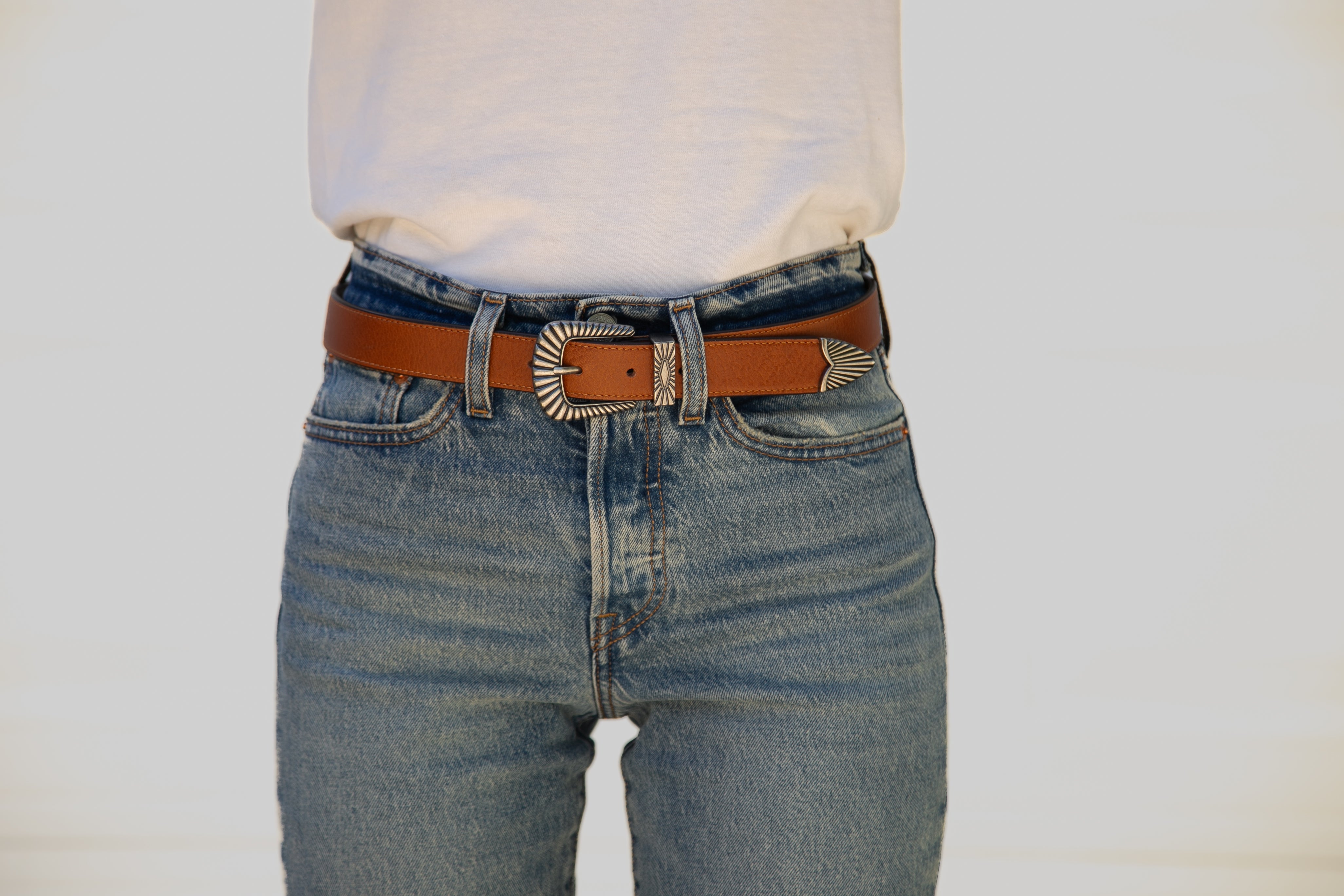 Person wearing blue jeans with a brown belt and white shirt on a plain background