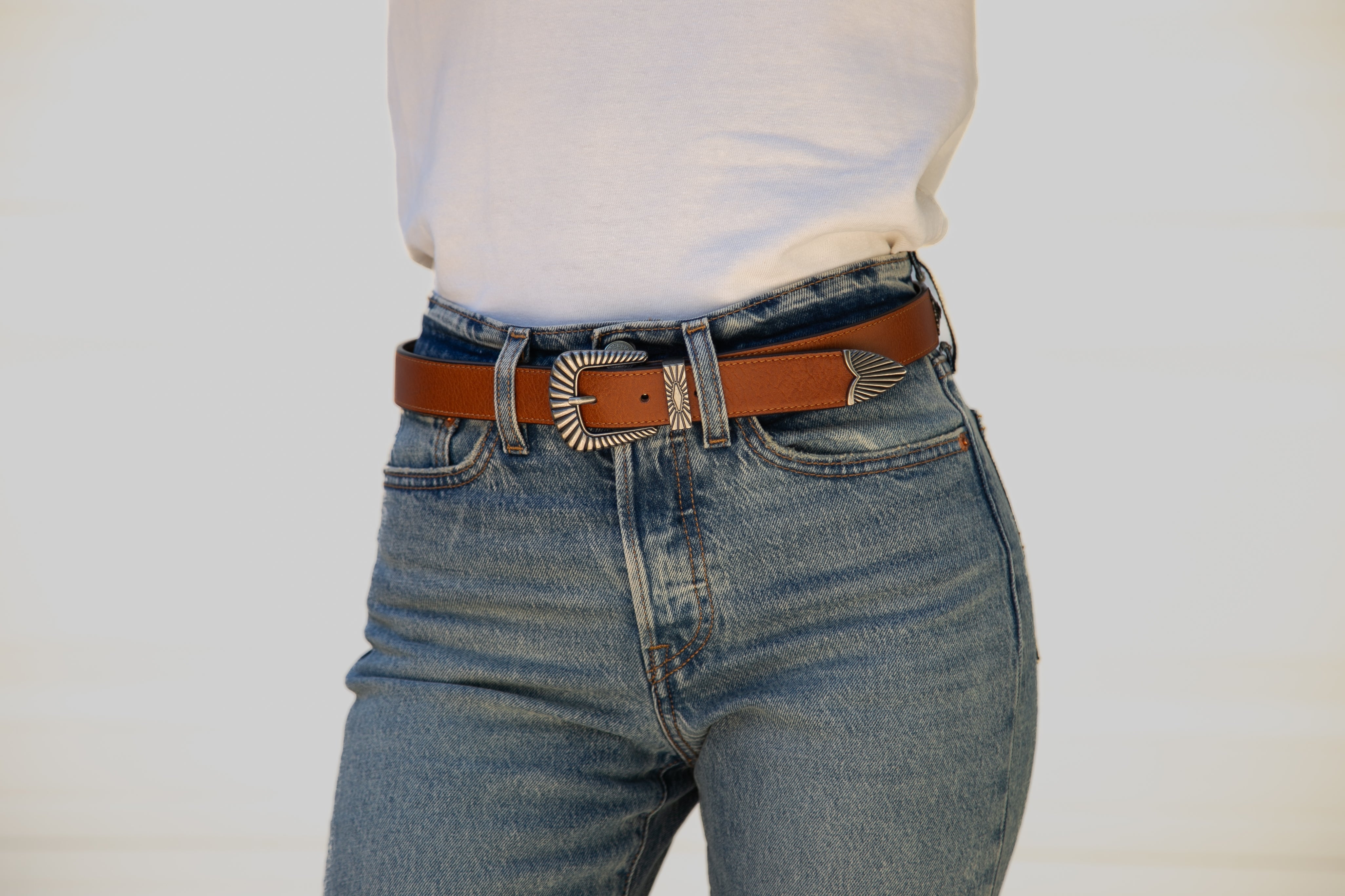Person wearing blue jeans with a brown belt on a plain background