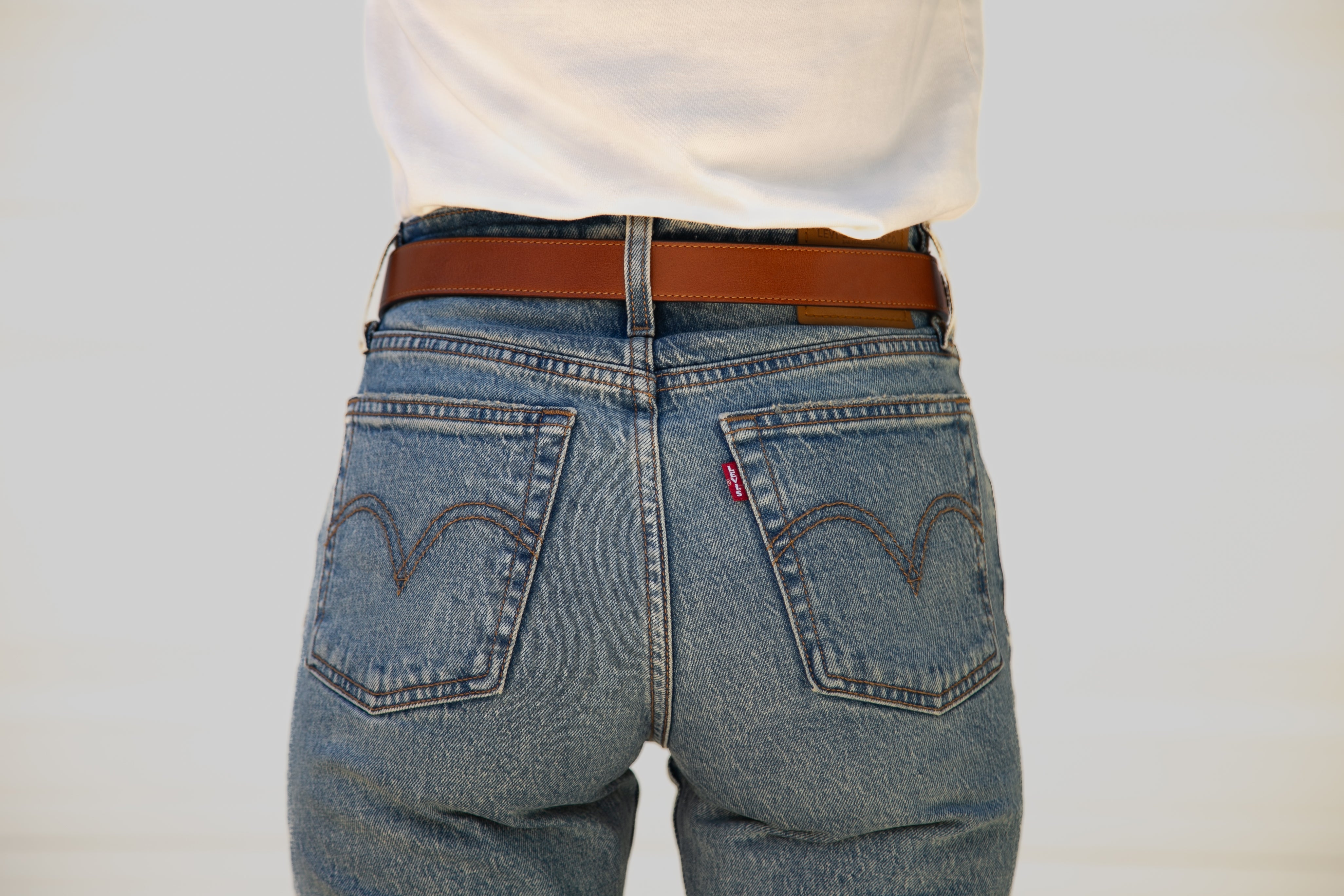 Blue jeans with a brown belt on a plain background