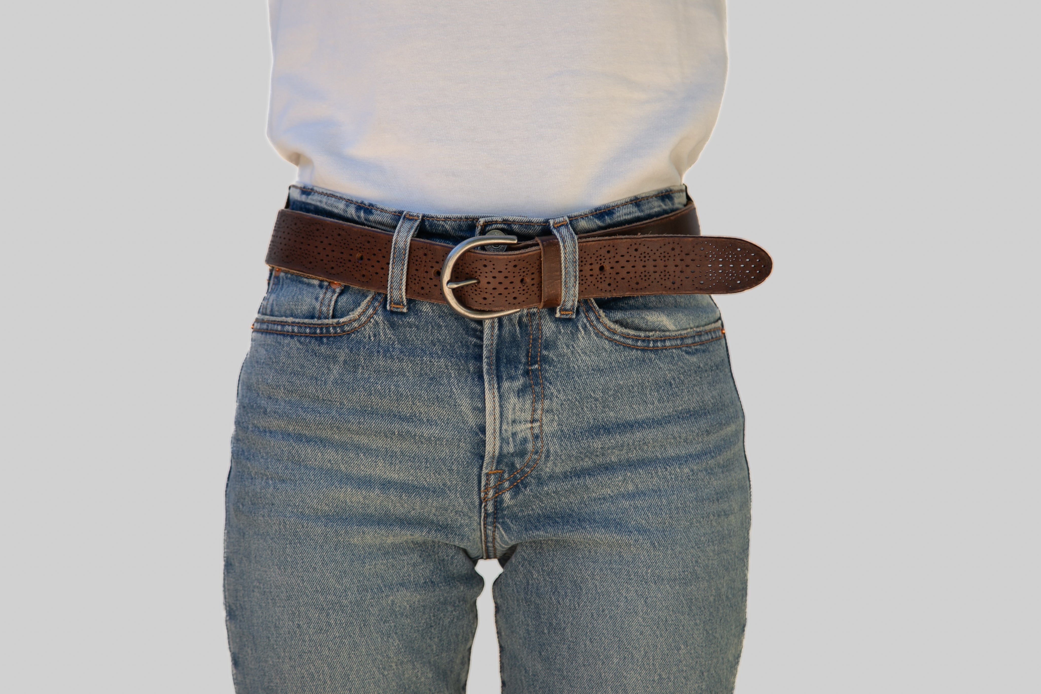 Person wearing blue jeans with a brown belt on a plain background
