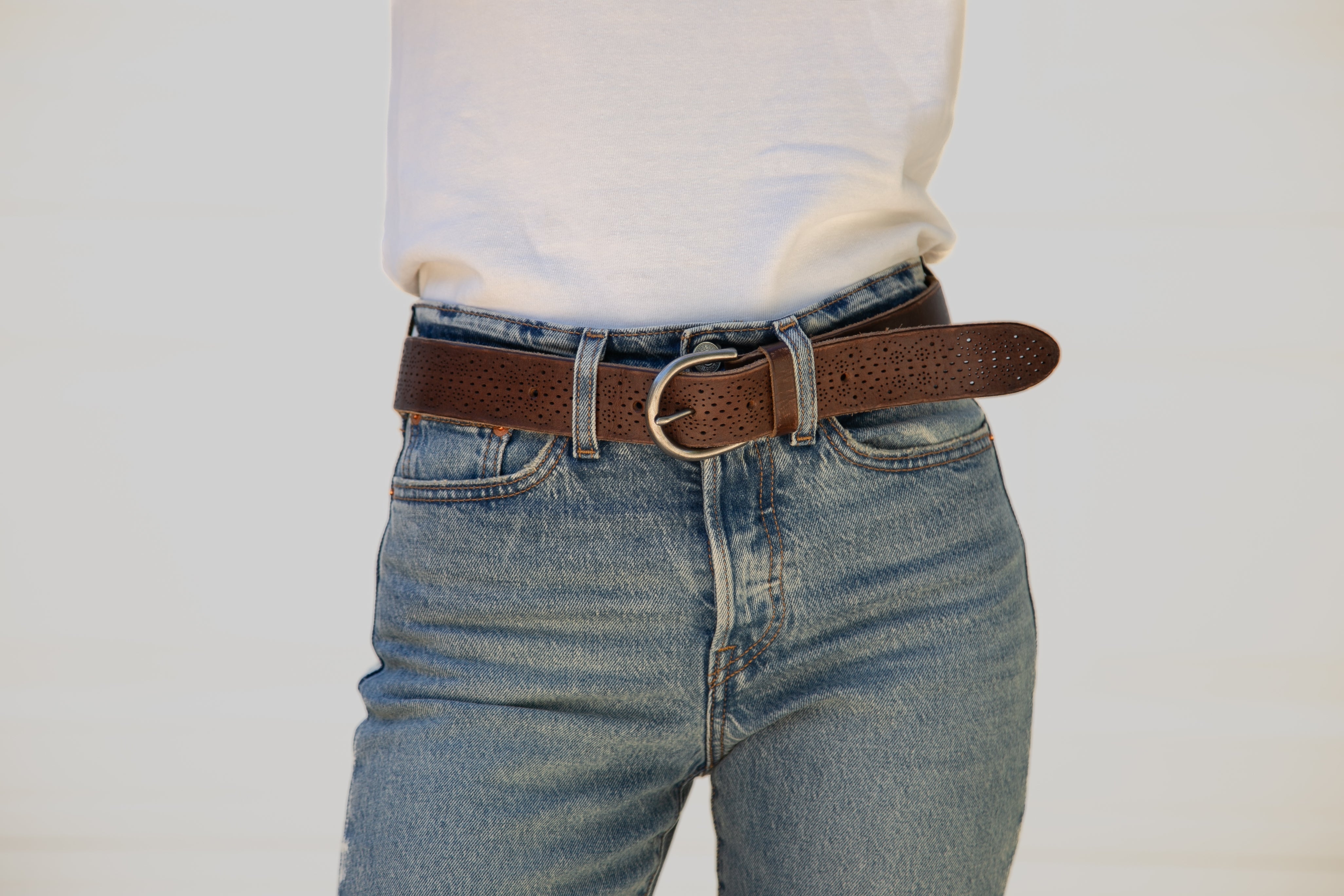 Person wearing blue jeans with a brown belt on a plain background