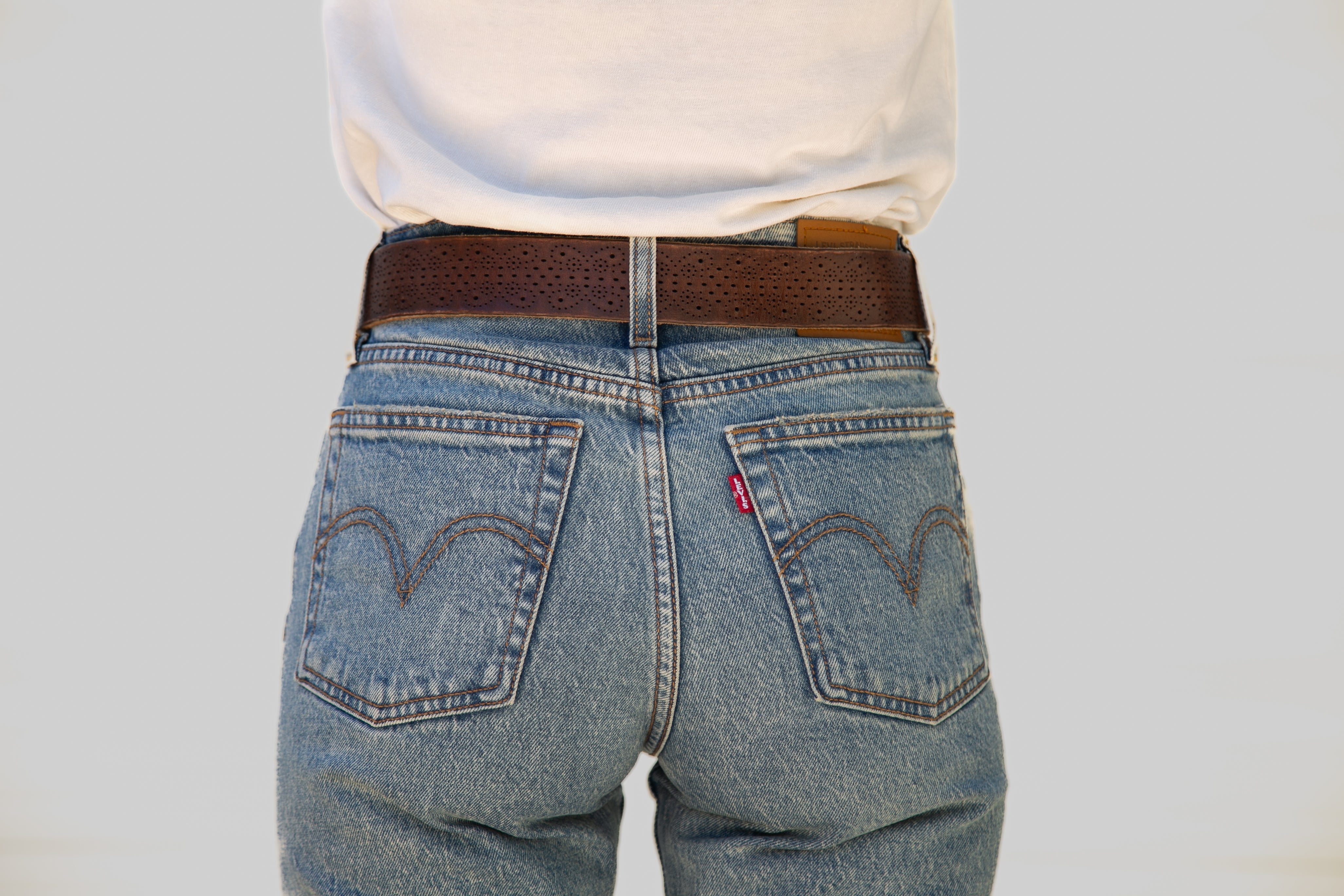 Person wearing blue jeans with a brown belt on a plain background
