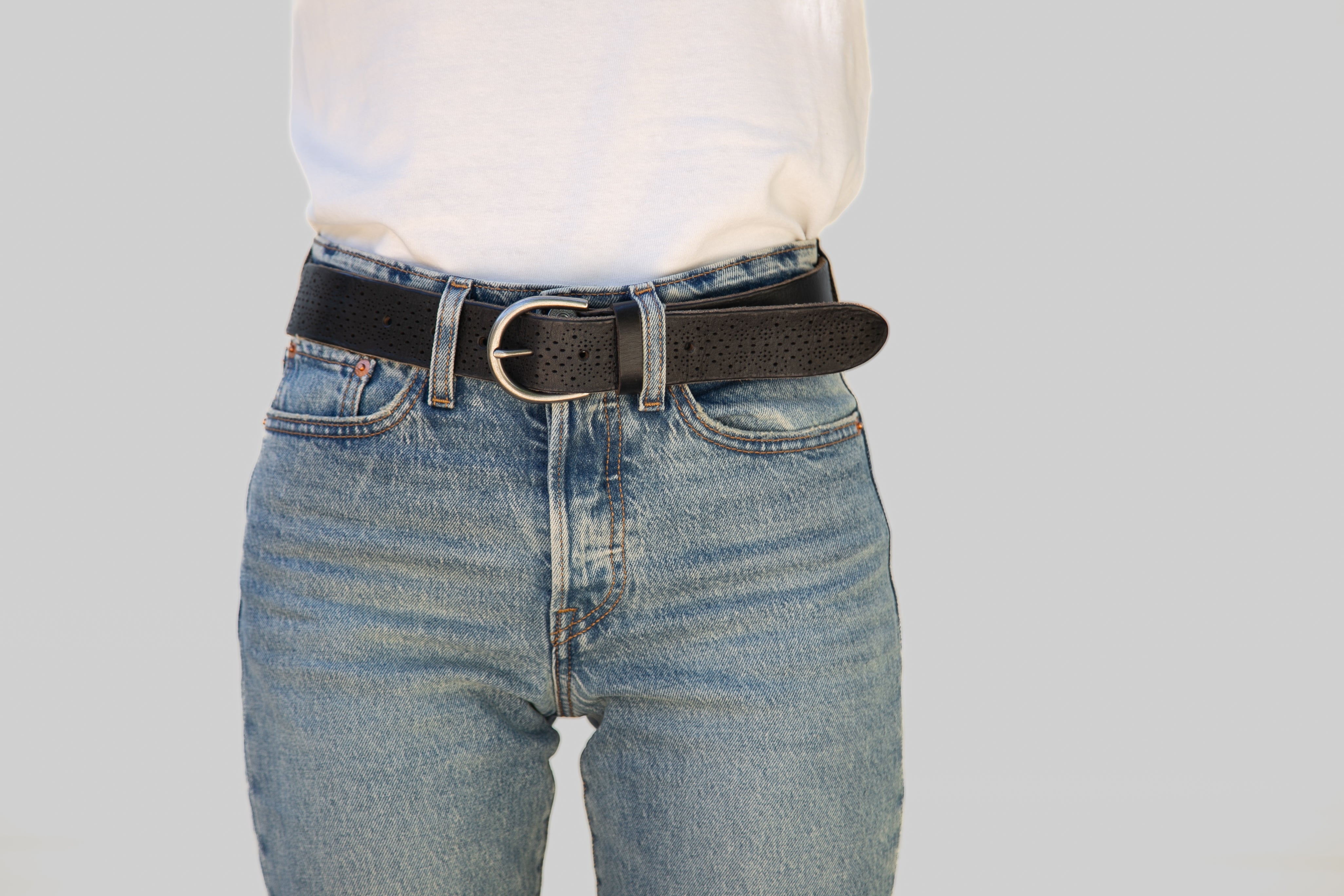 Person wearing blue jeans with a black belt on a light gray background
