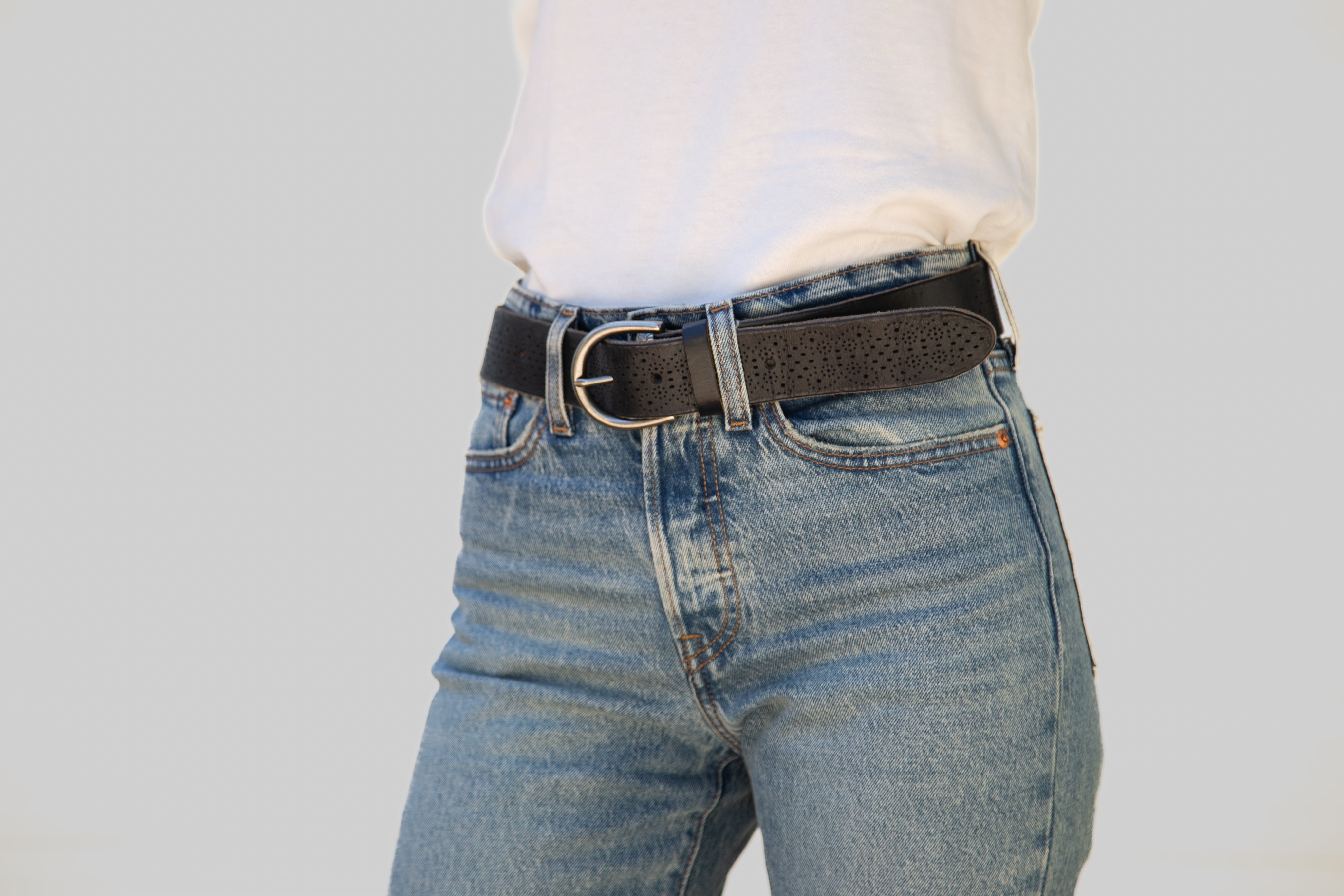 Person wearing blue jeans with a black belt on a plain background