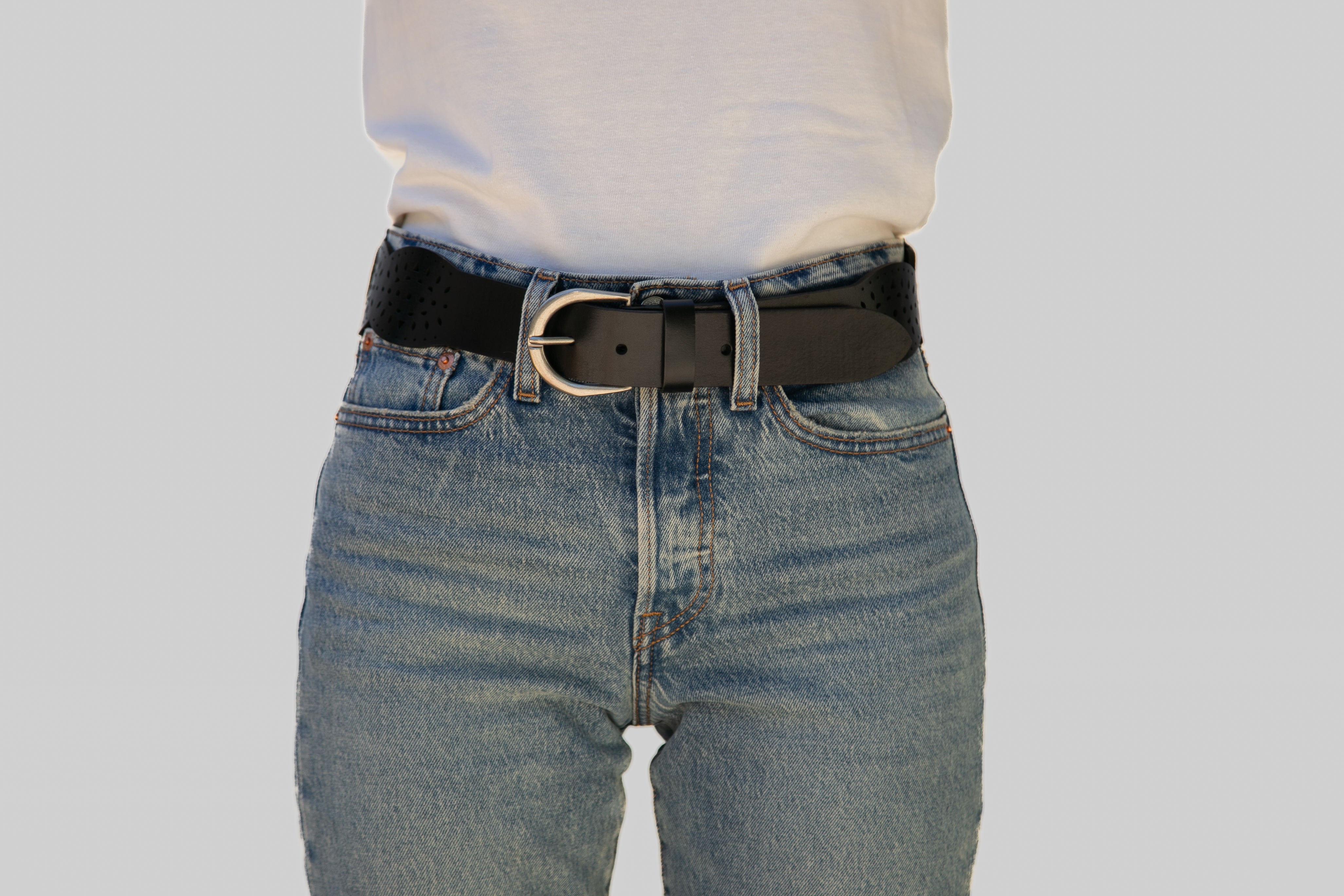 Person wearing blue jeans with a black belt on a plain background