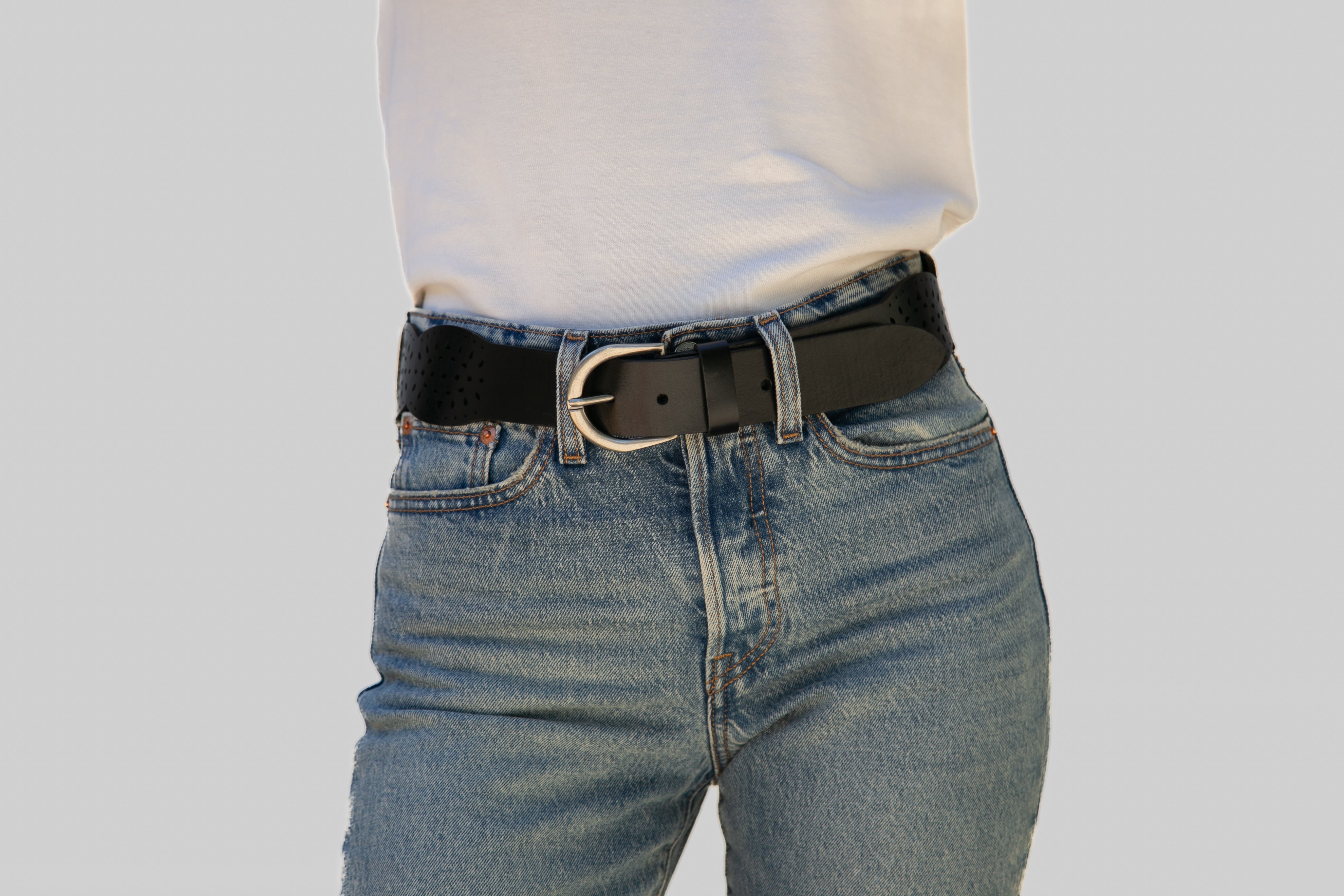 Person wearing a black belt with a silver buckle on blue jeans against a gray background