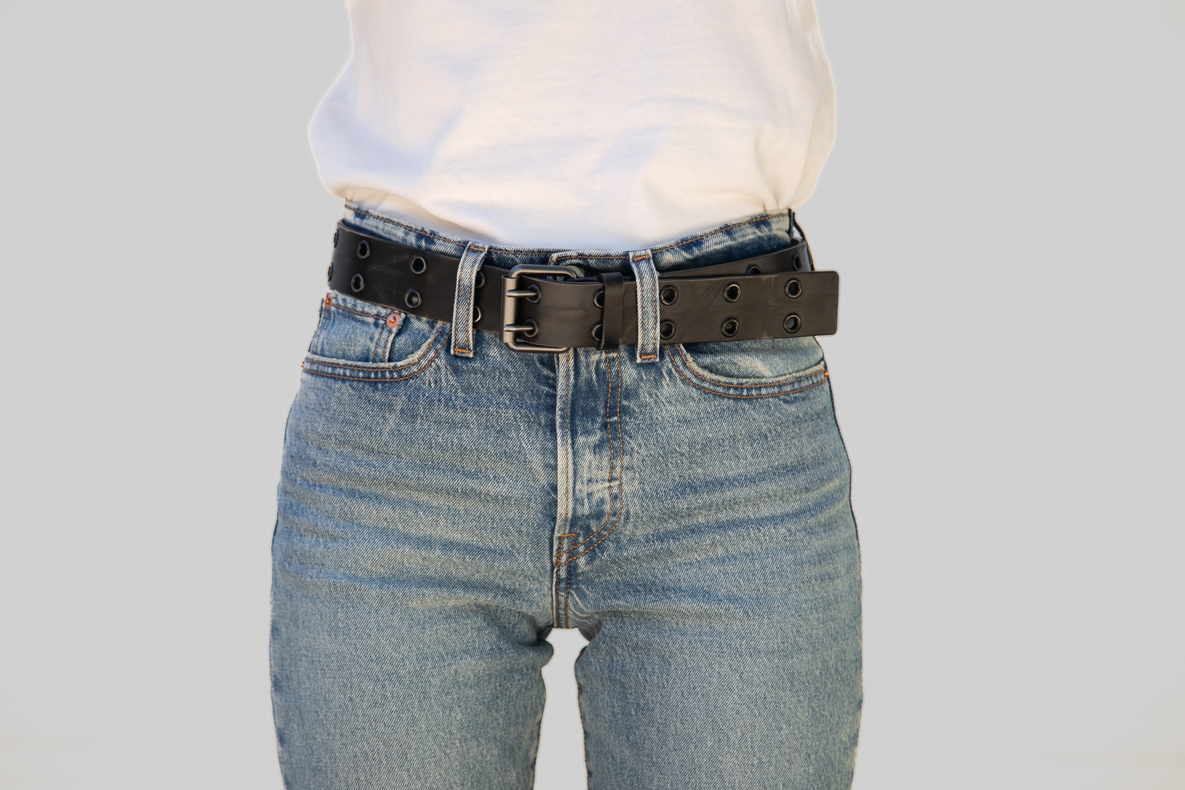Person wearing blue jeans with a black belt on a plain background