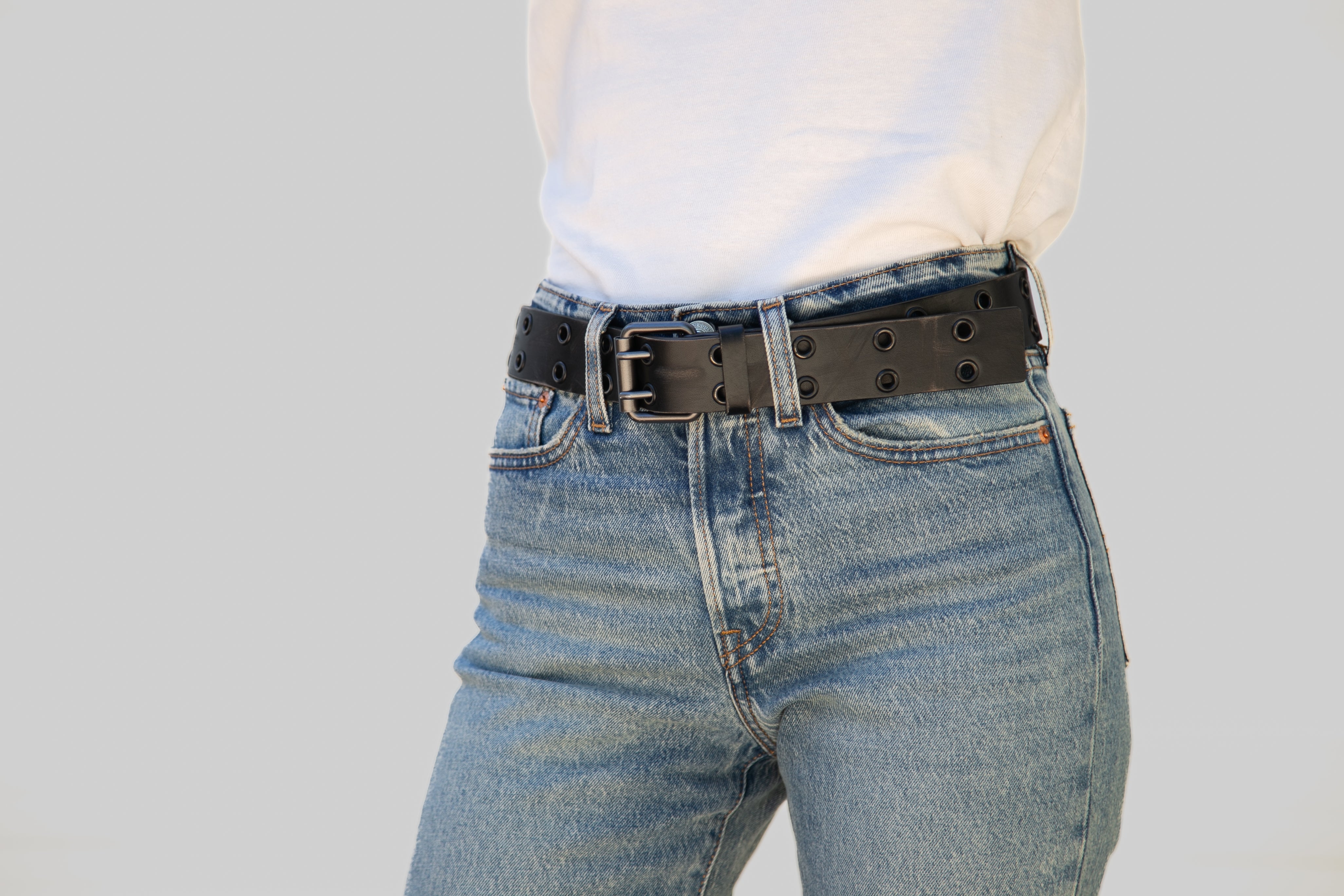 Person wearing blue jeans and a black belt on a plain background