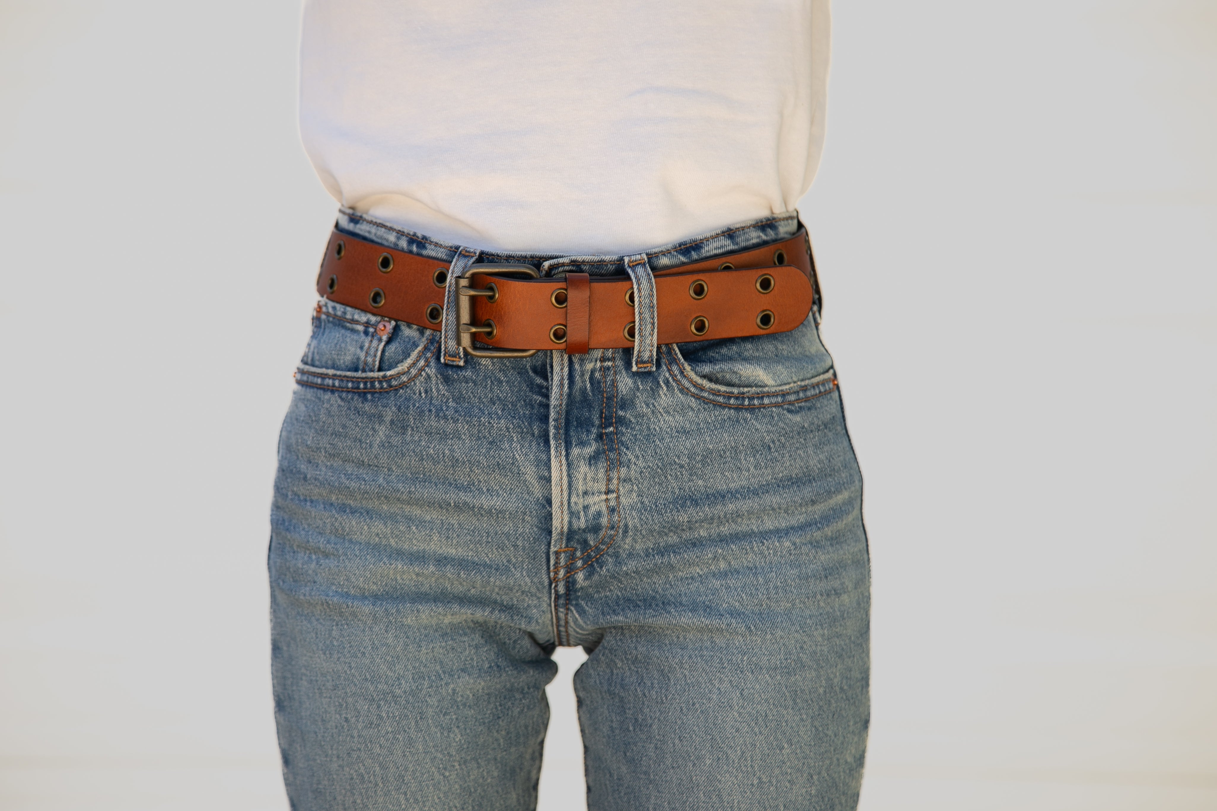 Person wearing blue jeans with a brown belt on a plain background