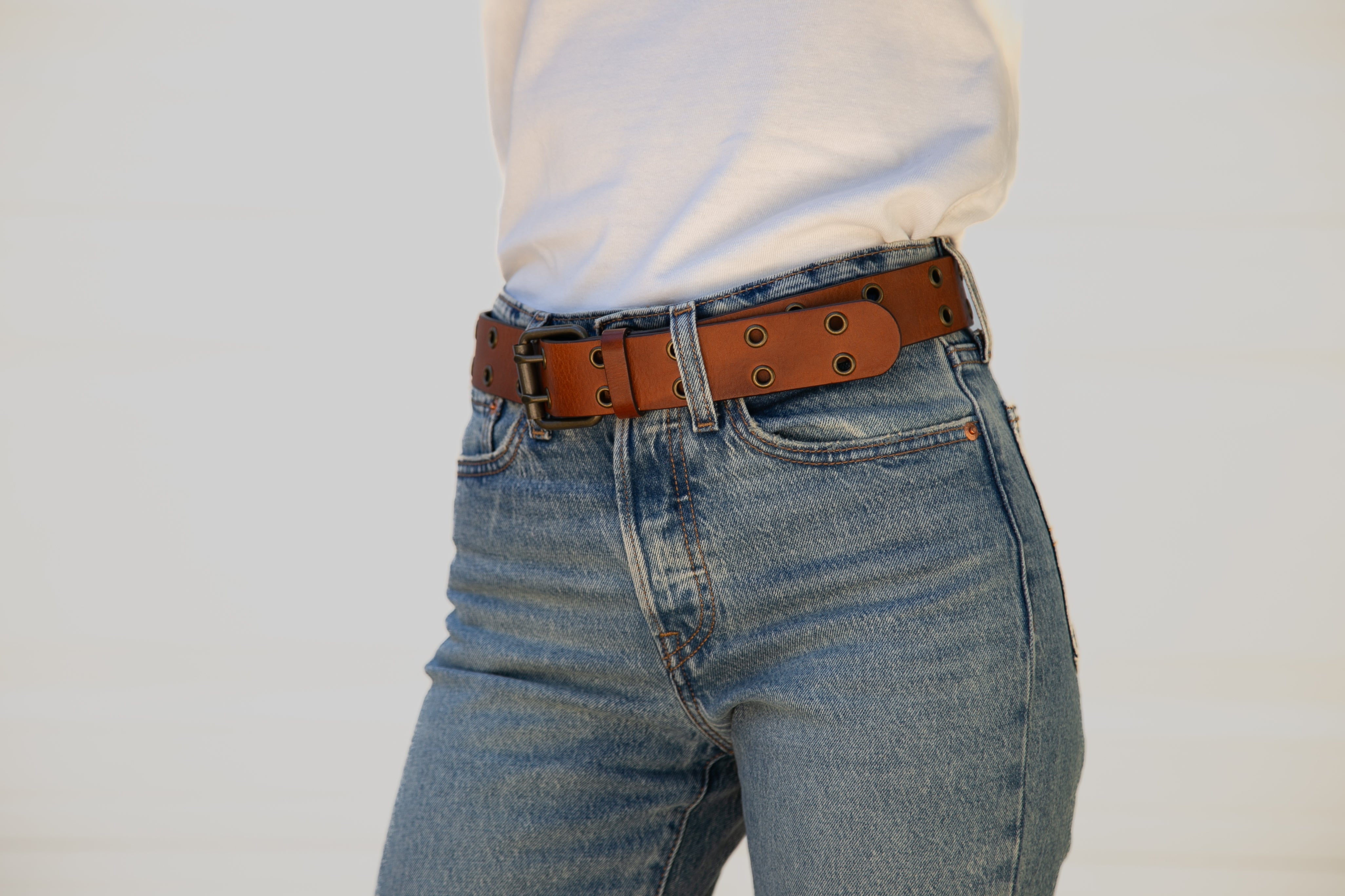 Person wearing blue jeans with a brown belt on a plain background