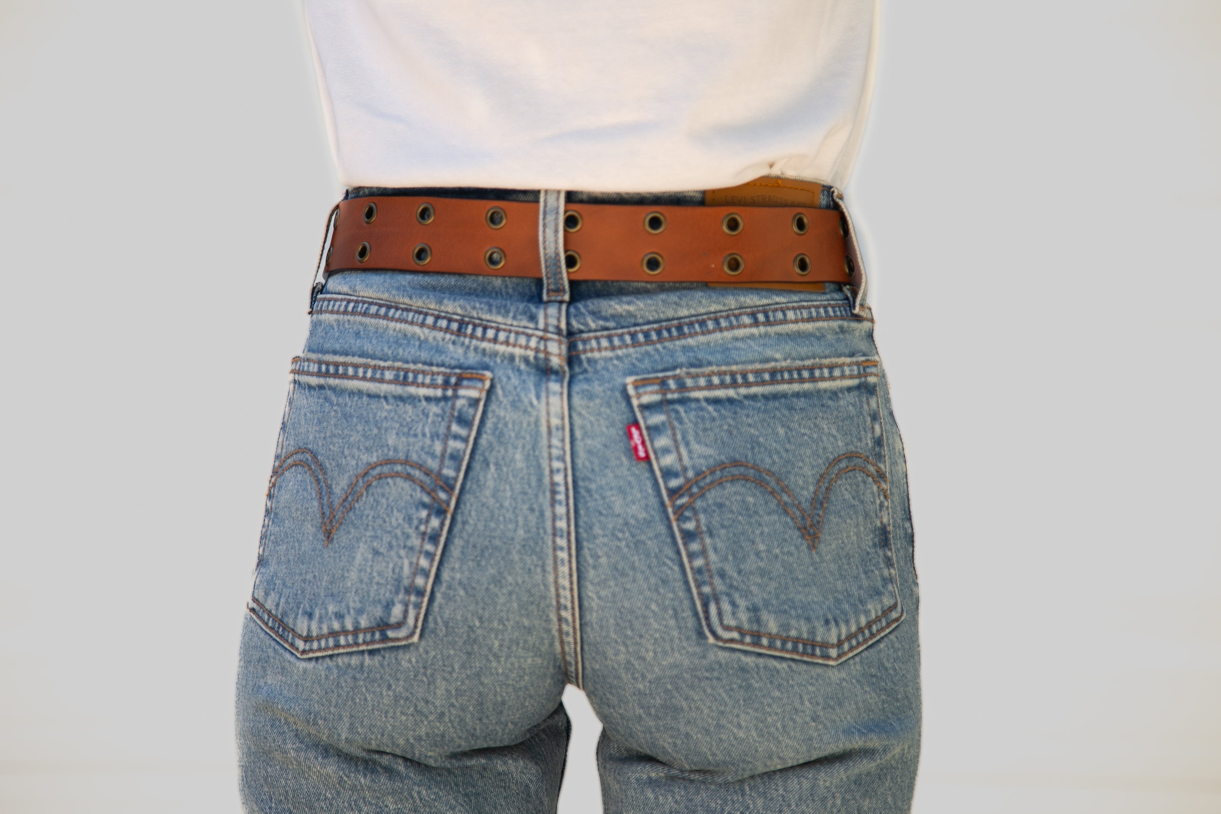 Blue jeans with a brown belt on a plain background