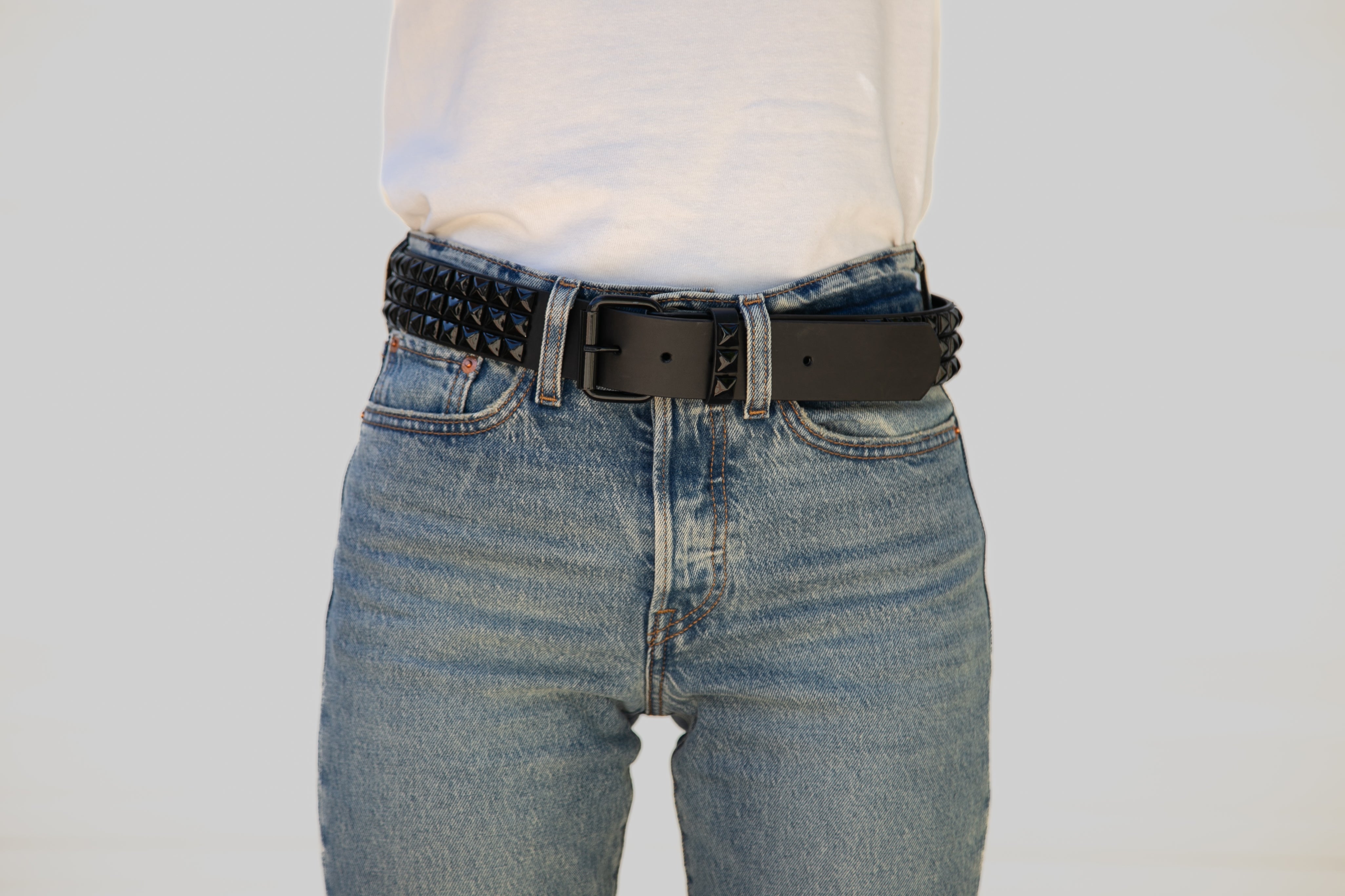 Person wearing blue jeans with a black belt on a plain background