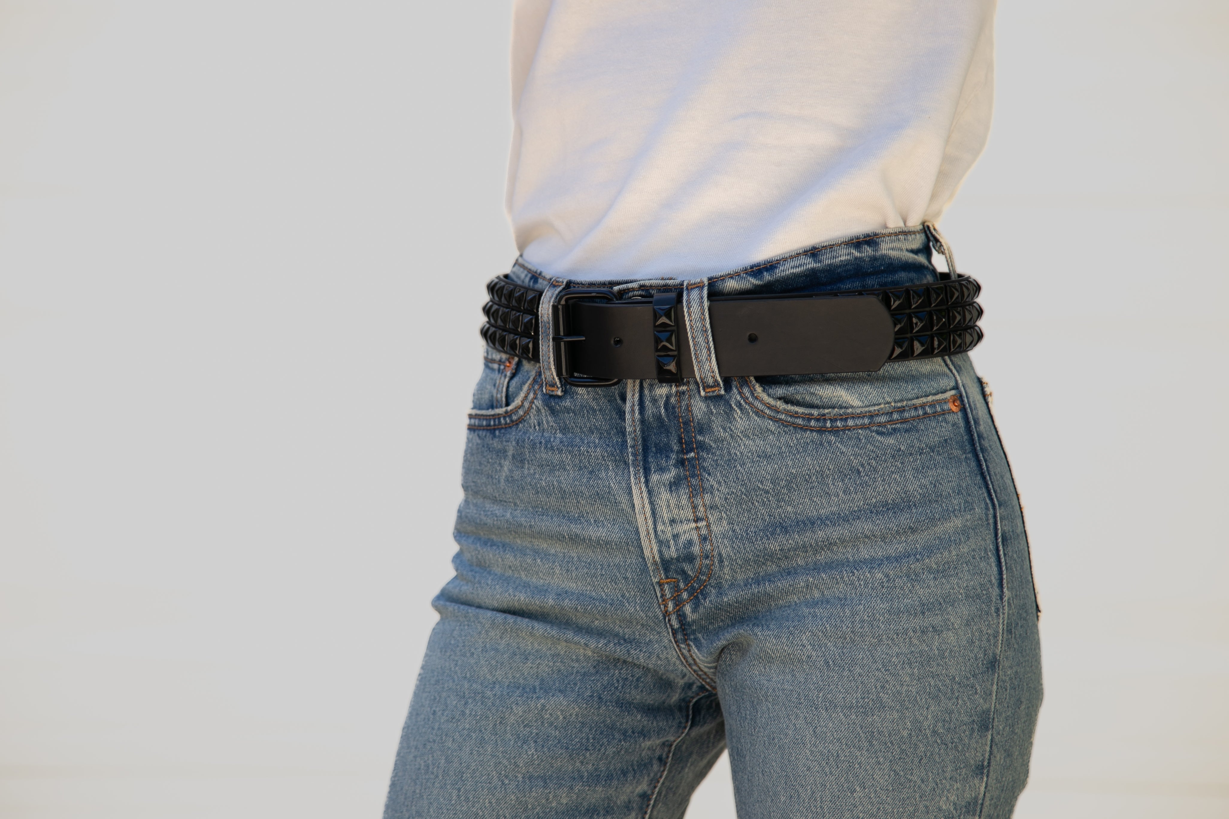 Person wearing blue jeans with a black belt on a plain background