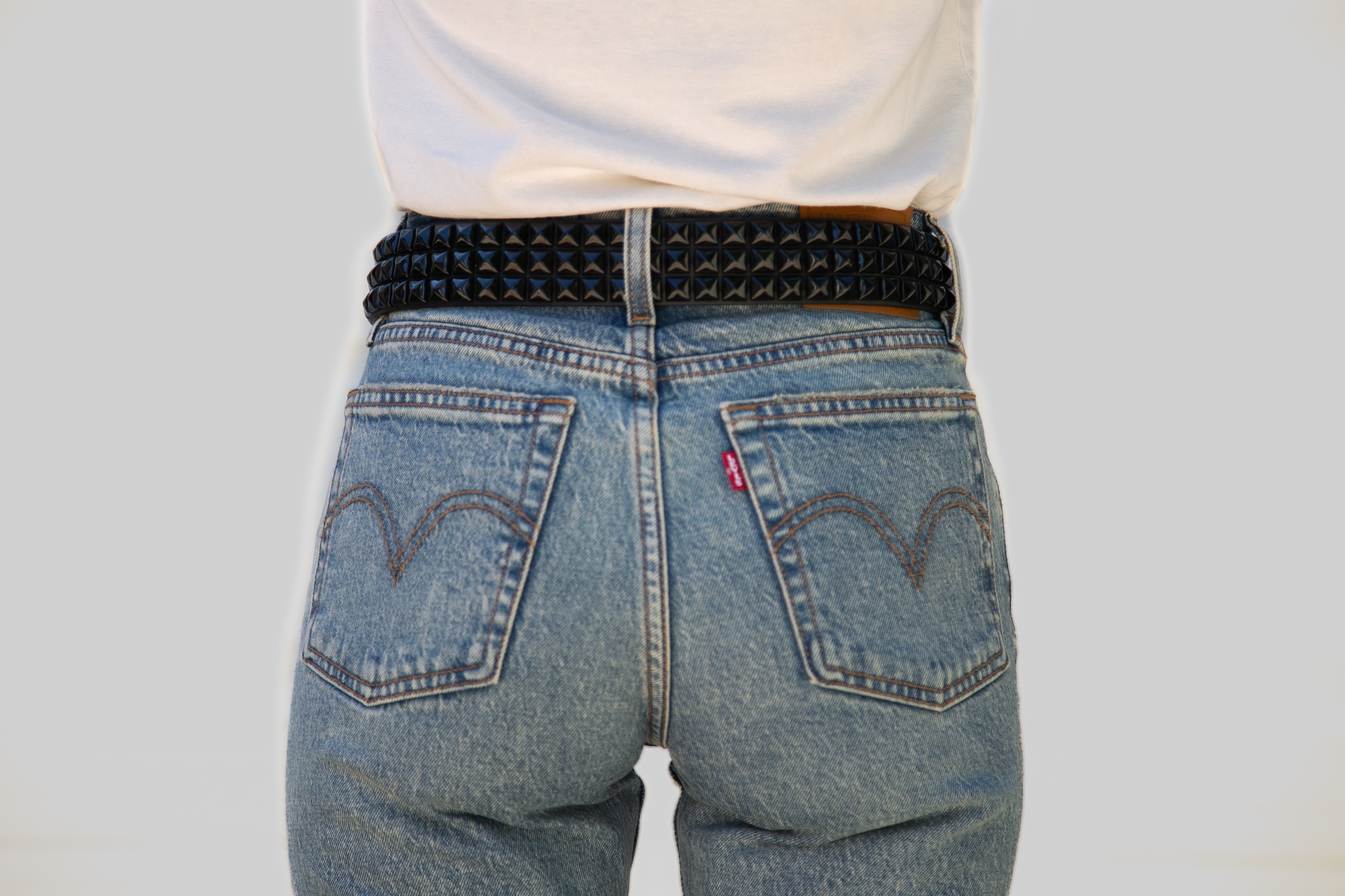 Person wearing blue jeans with a studded belt on a plain background