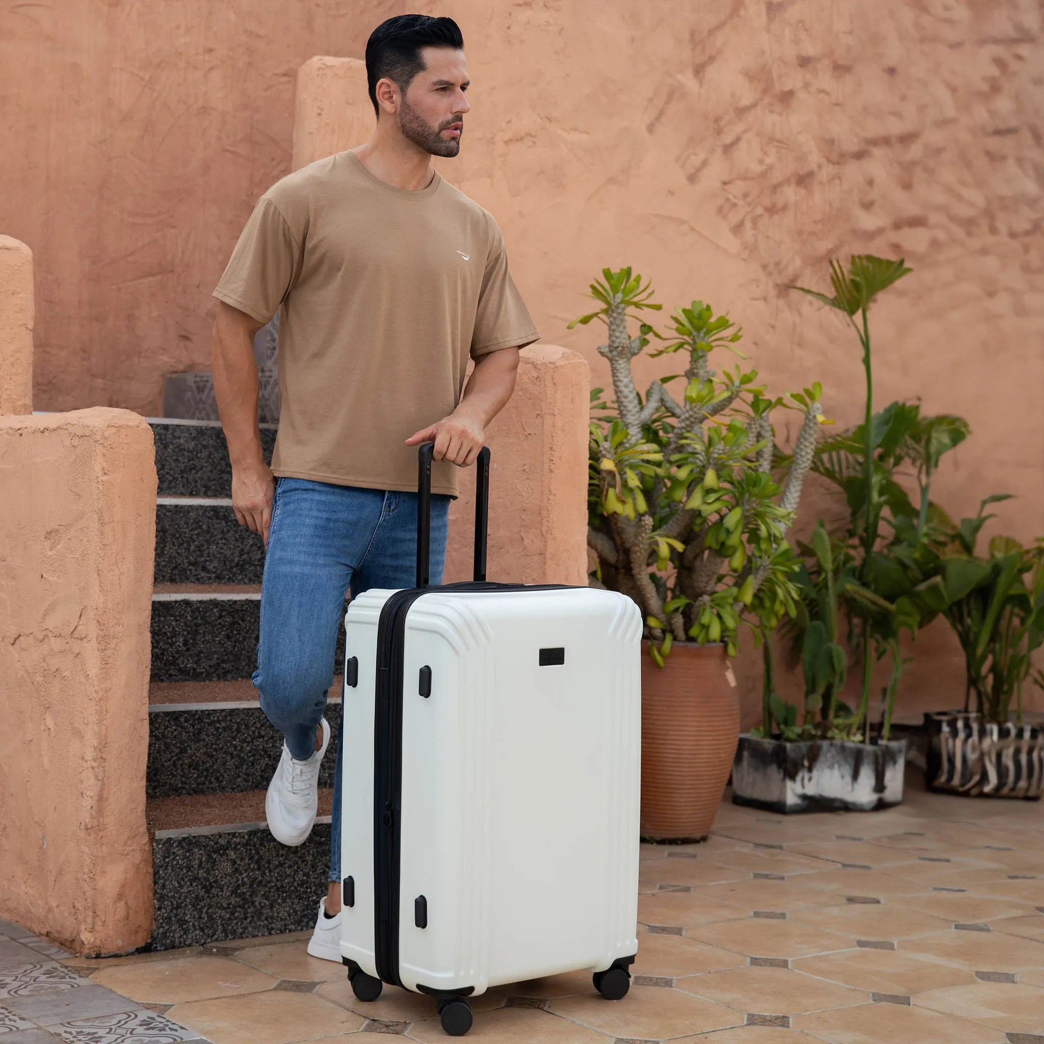 Man walking with a white suitcase in an outdoor setting with plants and stone steps.