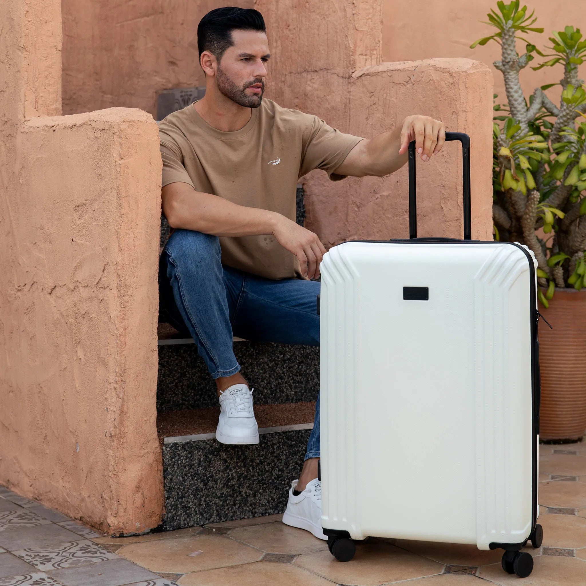 Man sitting on steps with a white suitcase in an outdoor setting