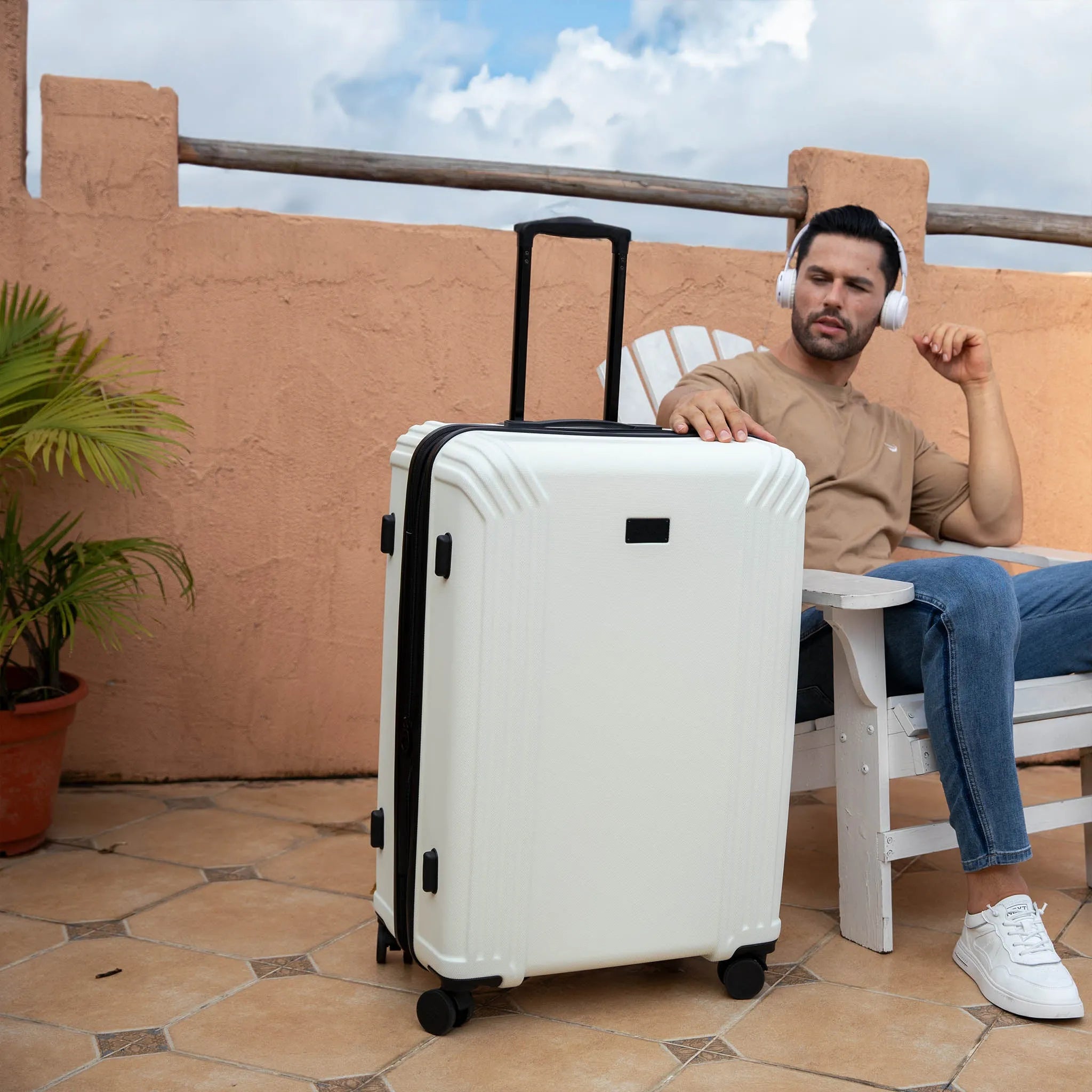 Man sitting on a chair with a white suitcase next to him on a rooftop.