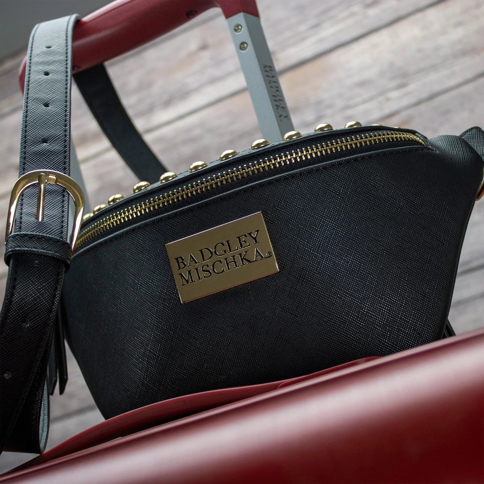 Black handbag with gold zipper and 'Badgley Mischka' logo on a wooden surface