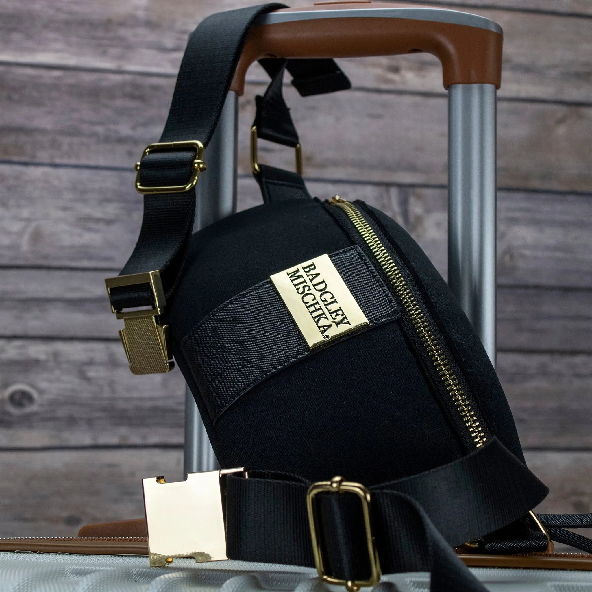 Black bag with gold accents on a suitcase against a wooden background