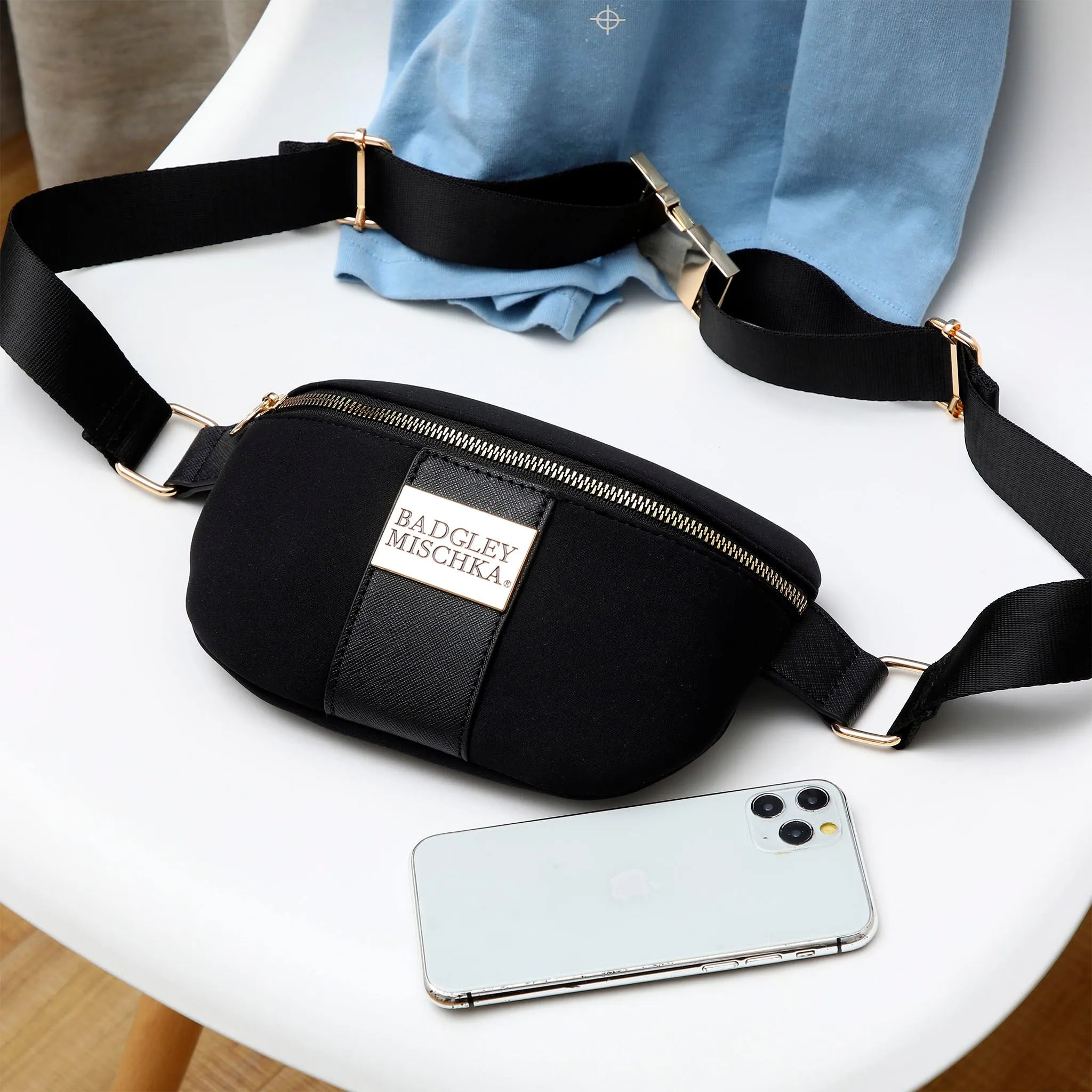 Black waist bag with 'Badgley Mischka' logo on a white surface with a phone next to it.