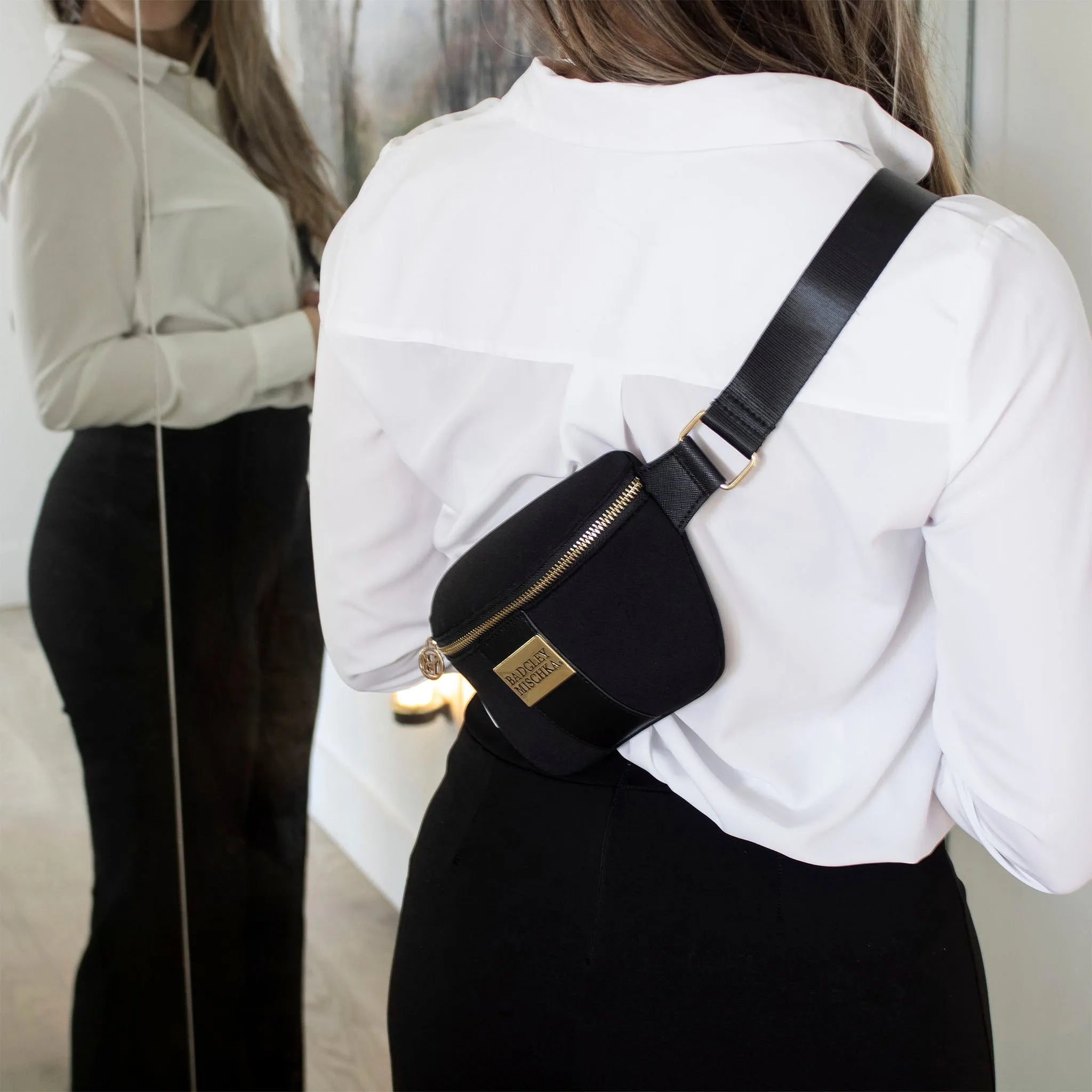 Person wearing a black waist bag with a gold zipper on a plain background
