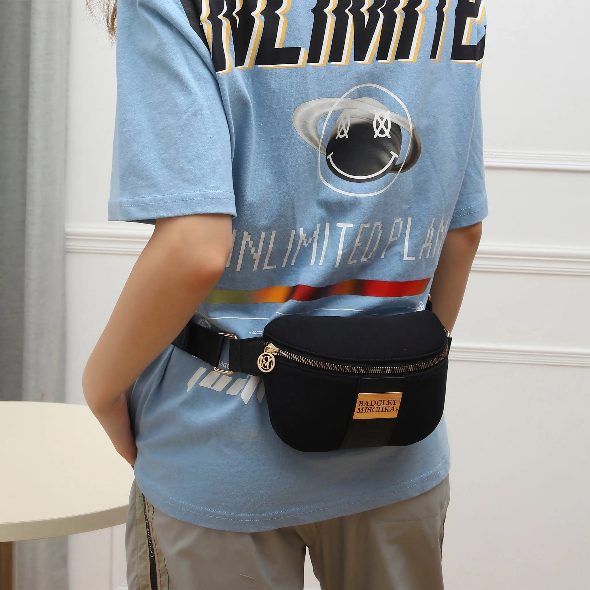 Person wearing a blue t-shirt with a graphic design and a black waist bag.
