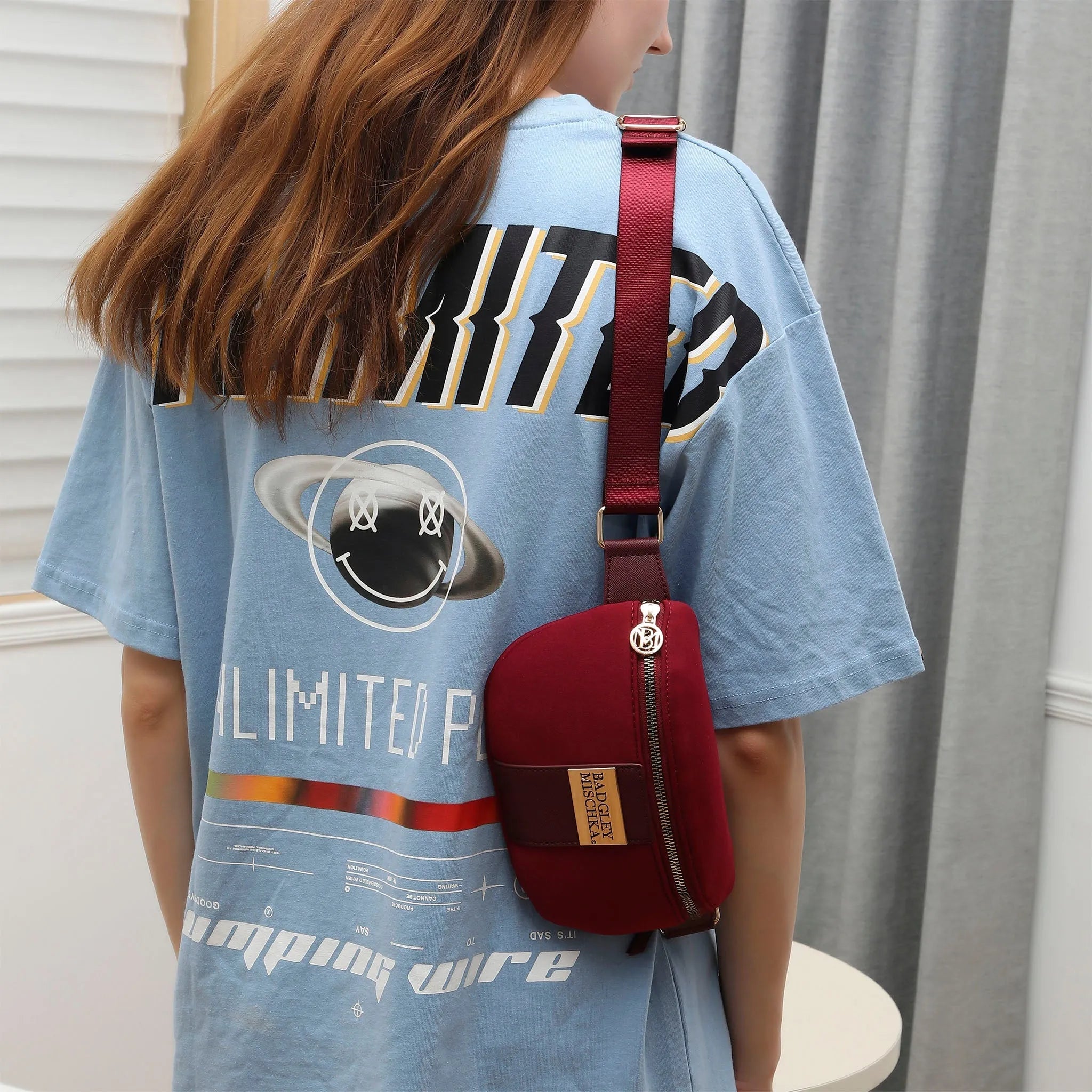 Person wearing a blue t-shirt with a graphic design and carrying a red bag.