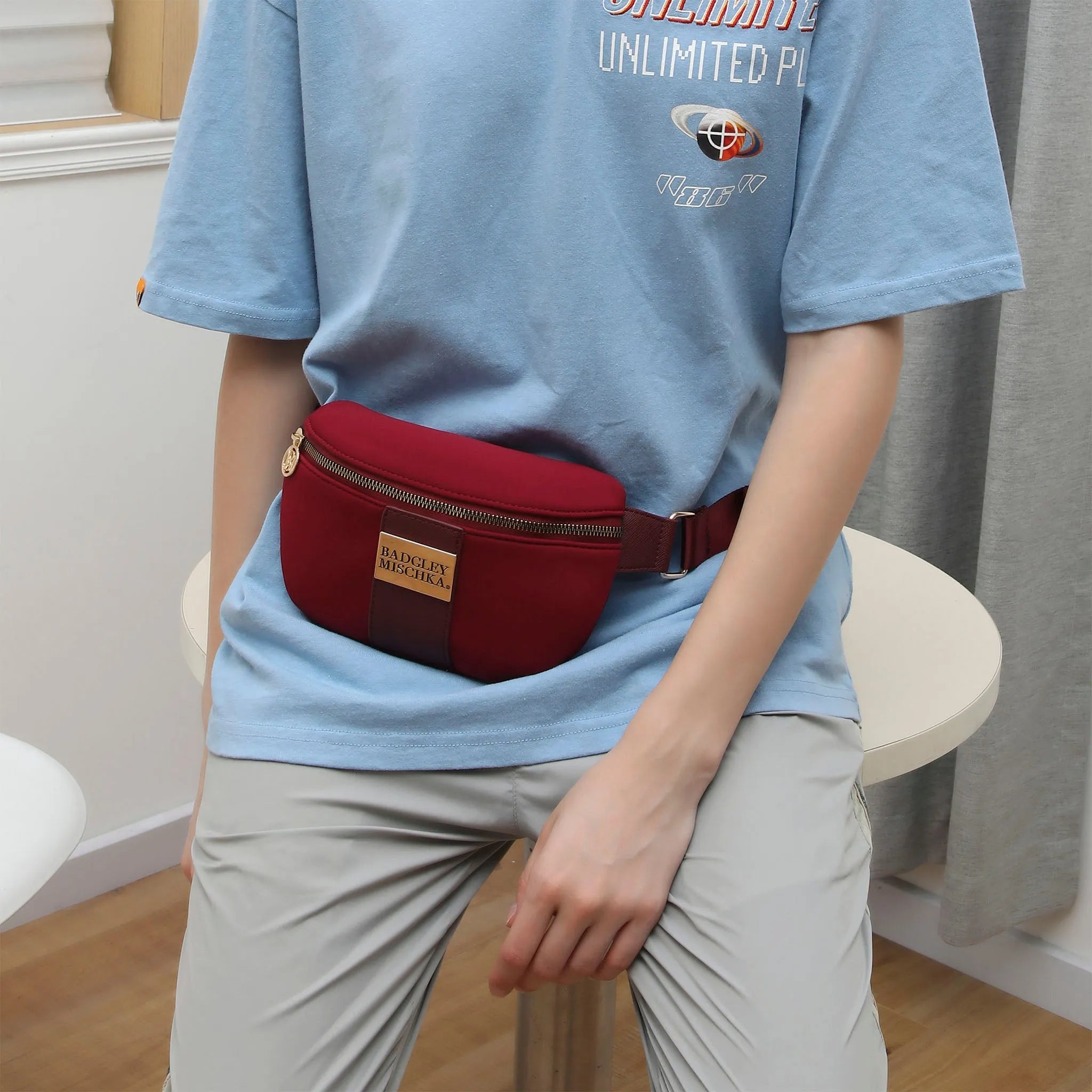 Person wearing a red waist bag with a visible brand logo, sitting on a chair indoors.