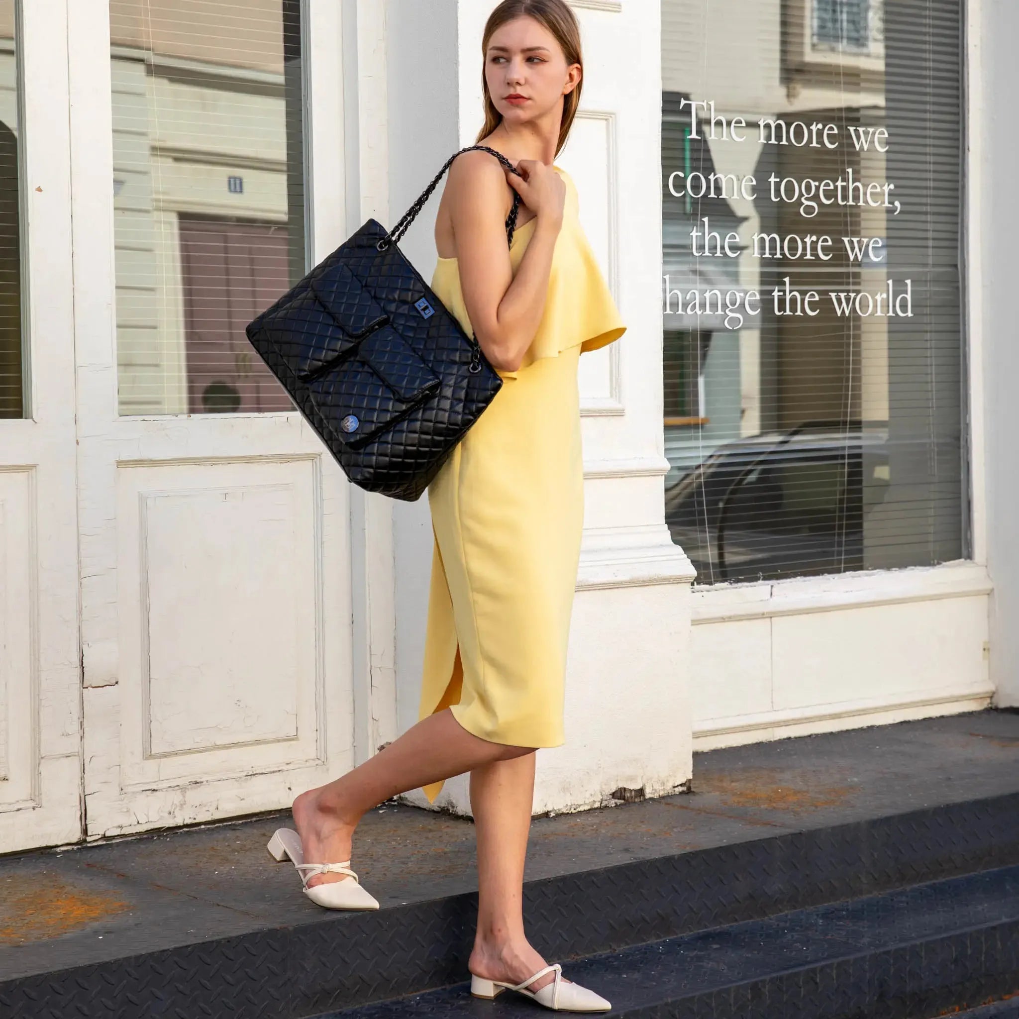 Woman in a yellow dress holding a black handbag on a city street.