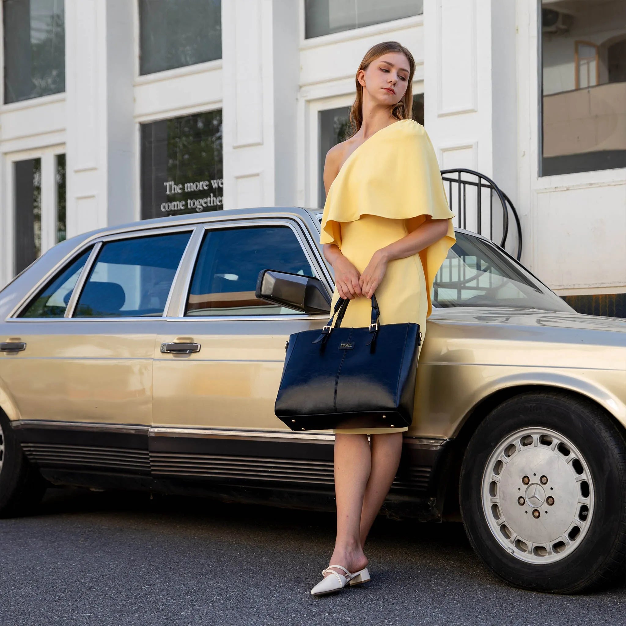 Woman in a yellow dress holding a blue handbag next to a vintage car.