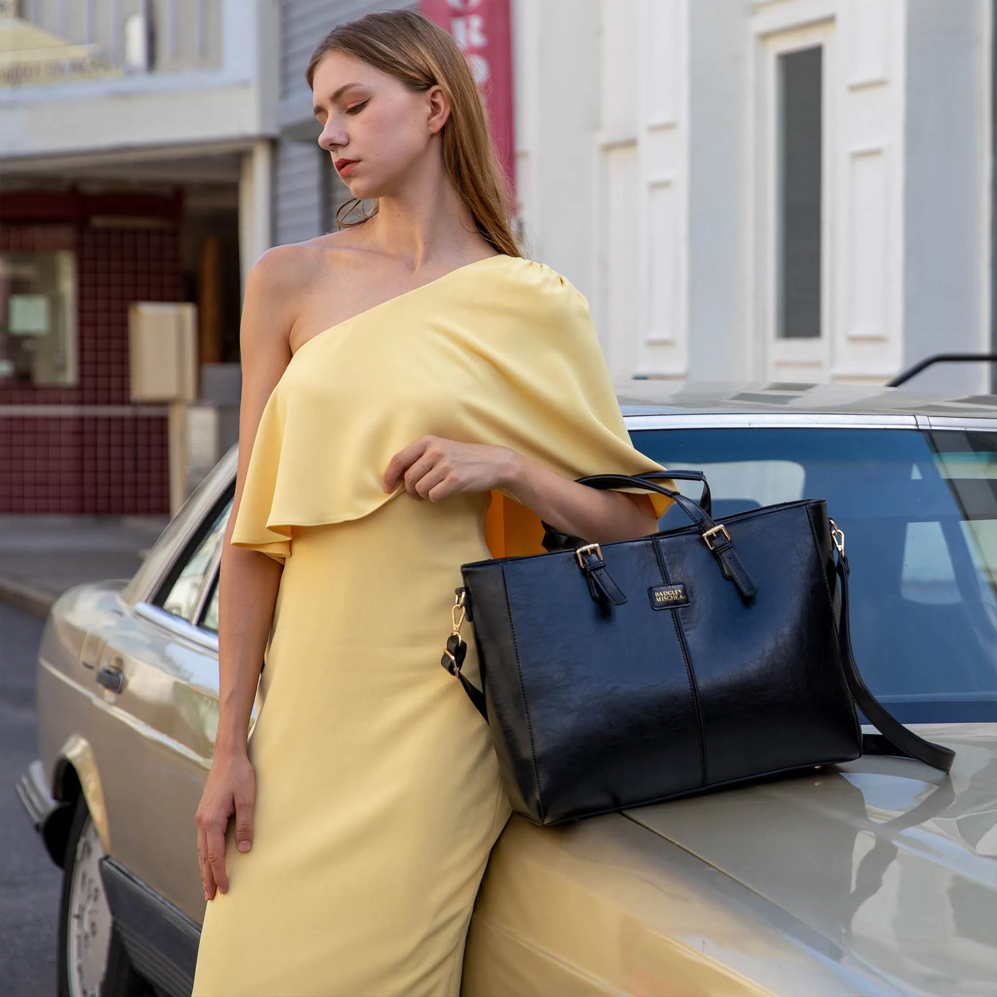 Woman in a yellow dress holding a blue handbag next to a vintage car.