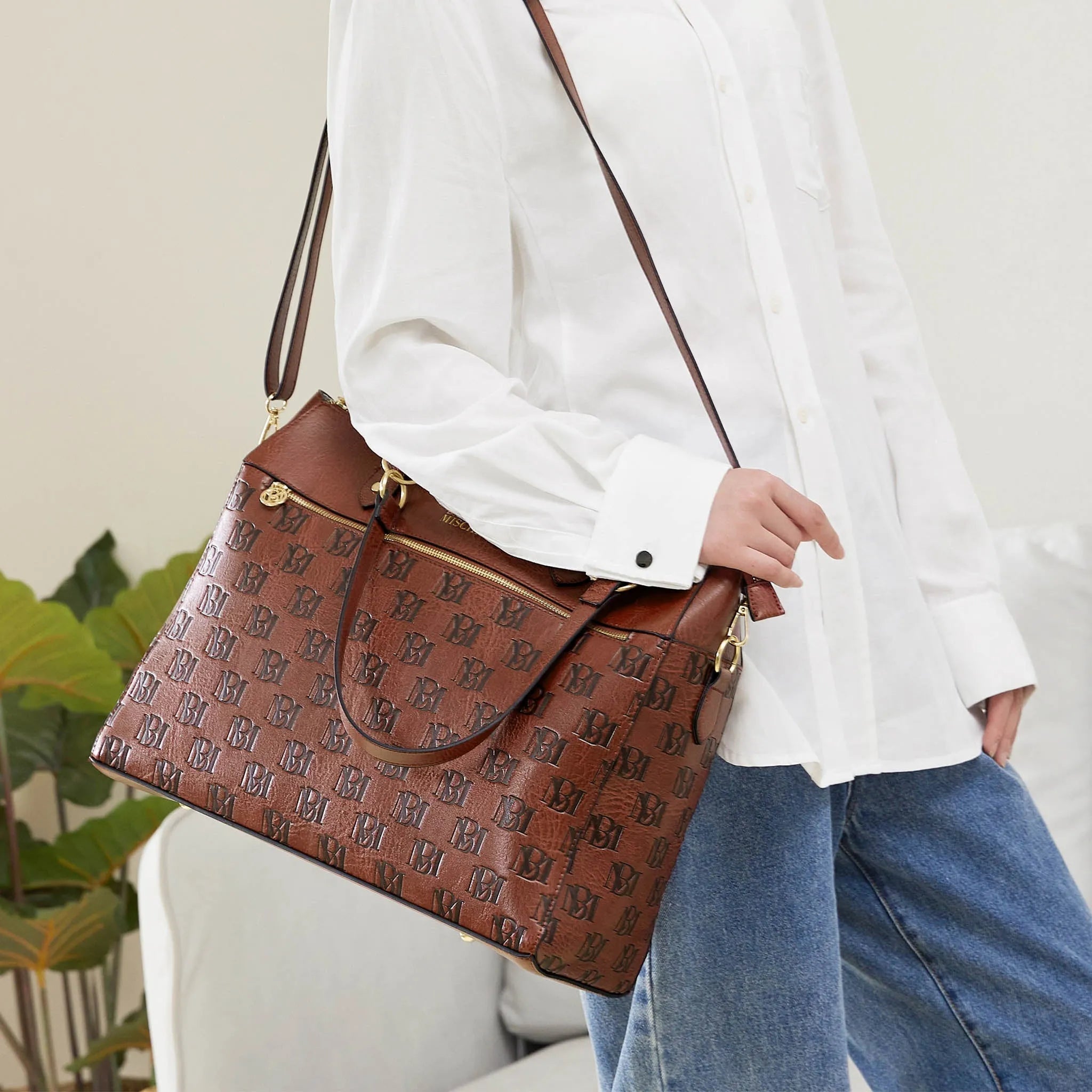 Person holding a brown patterned handbag with a white shirt and blue jeans.