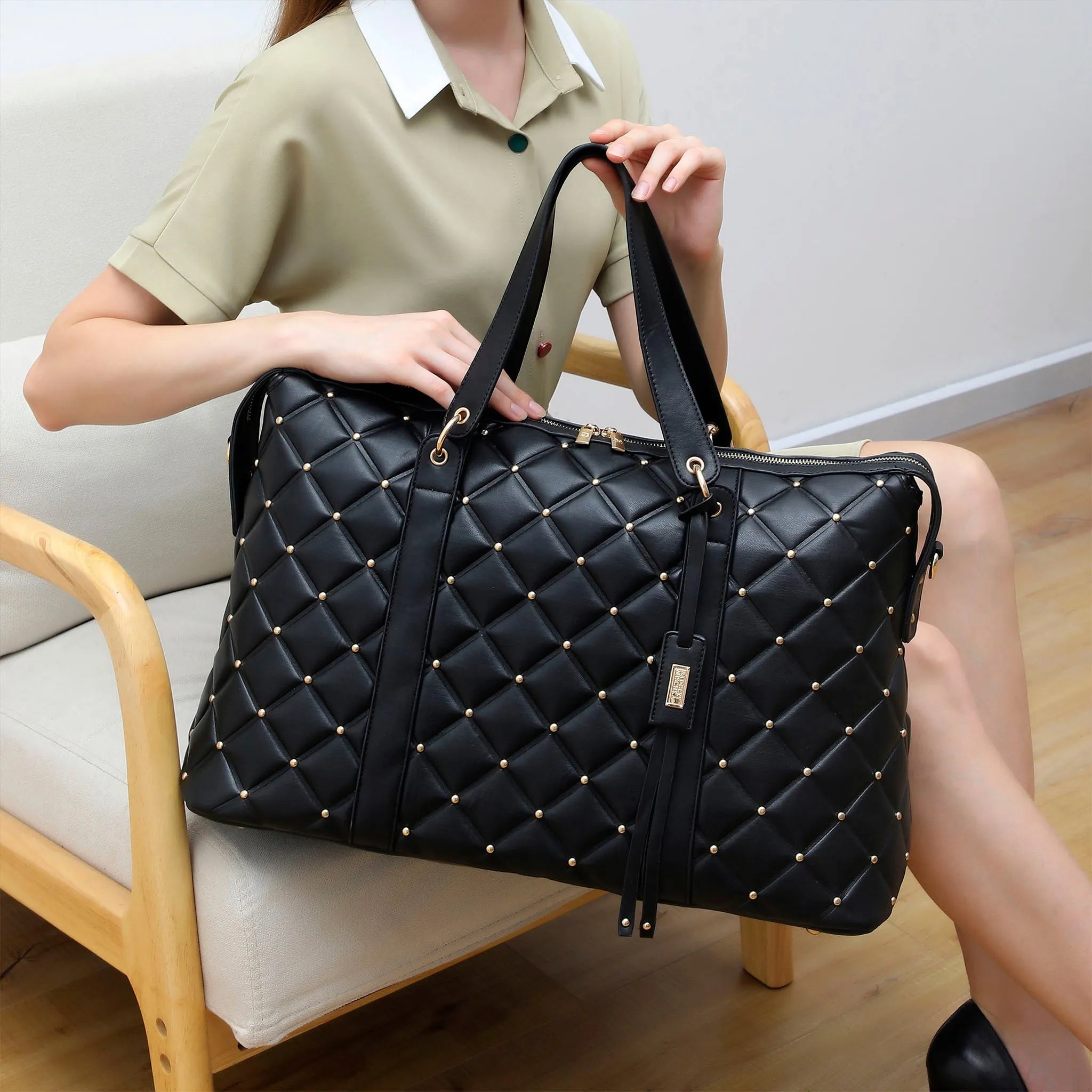 Person holding a black quilted handbag with gold studs in a casual setting.