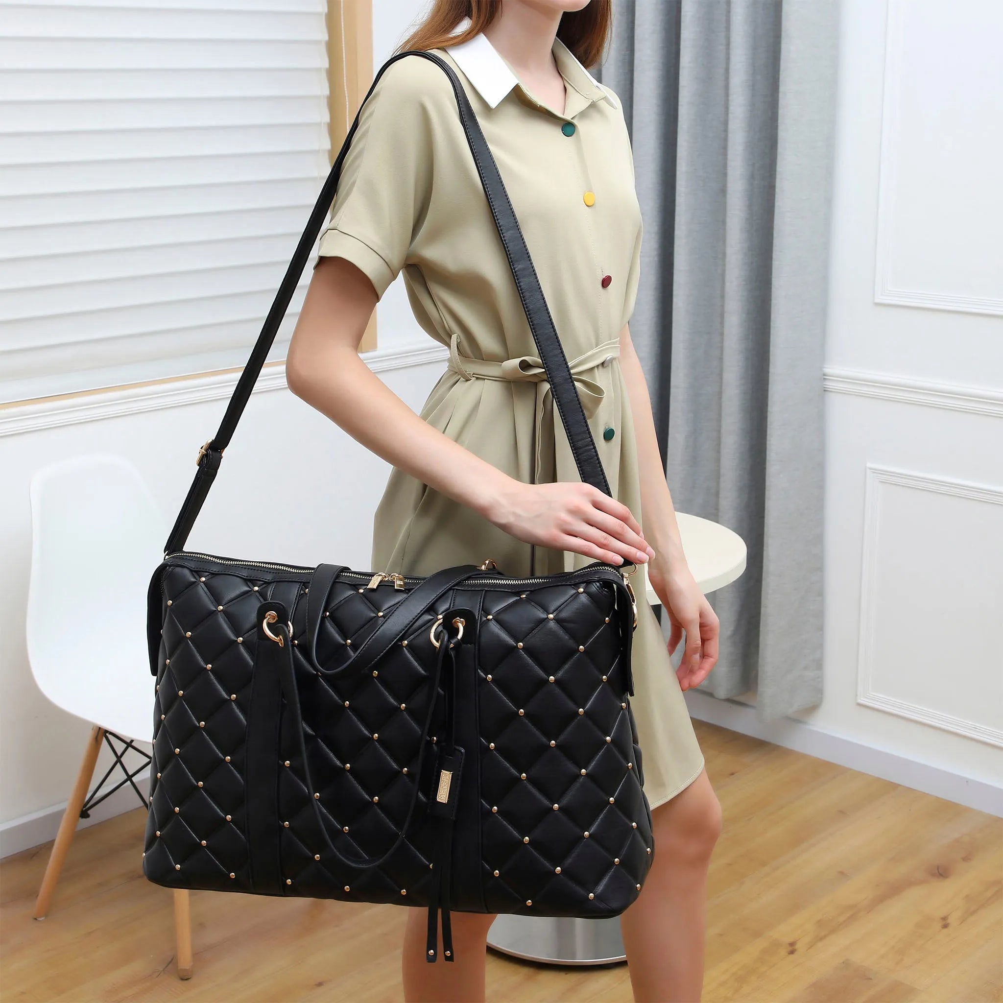 Person holding a black quilted handbag in a room with white walls and wooden floor.