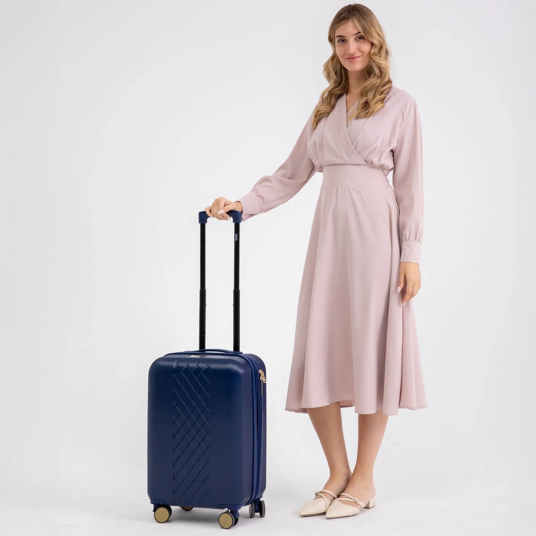 Woman in a pink dress holding a navy suitcase on a white background